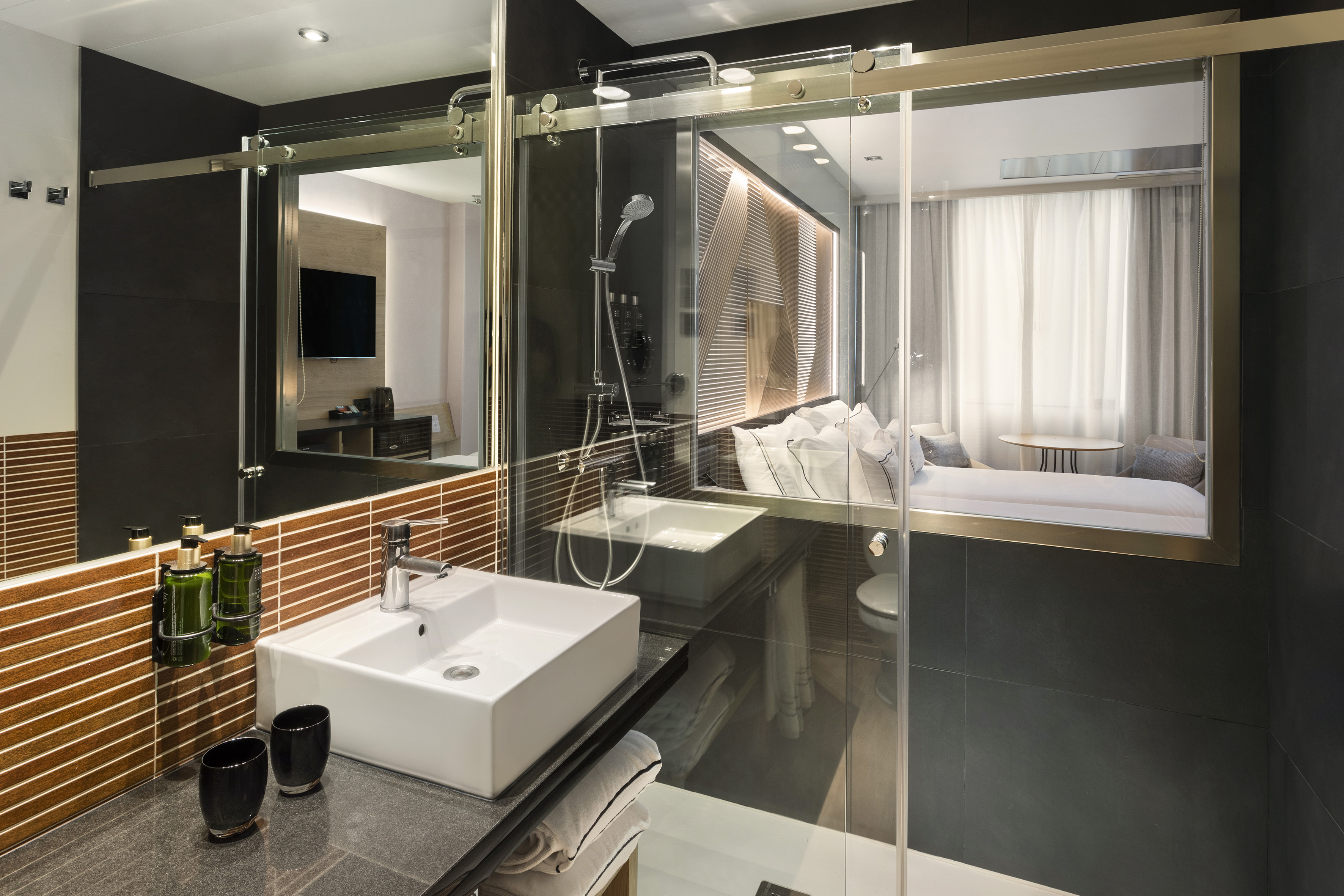Sleek hotel bathroom with glass shower partition to modern bedroom.