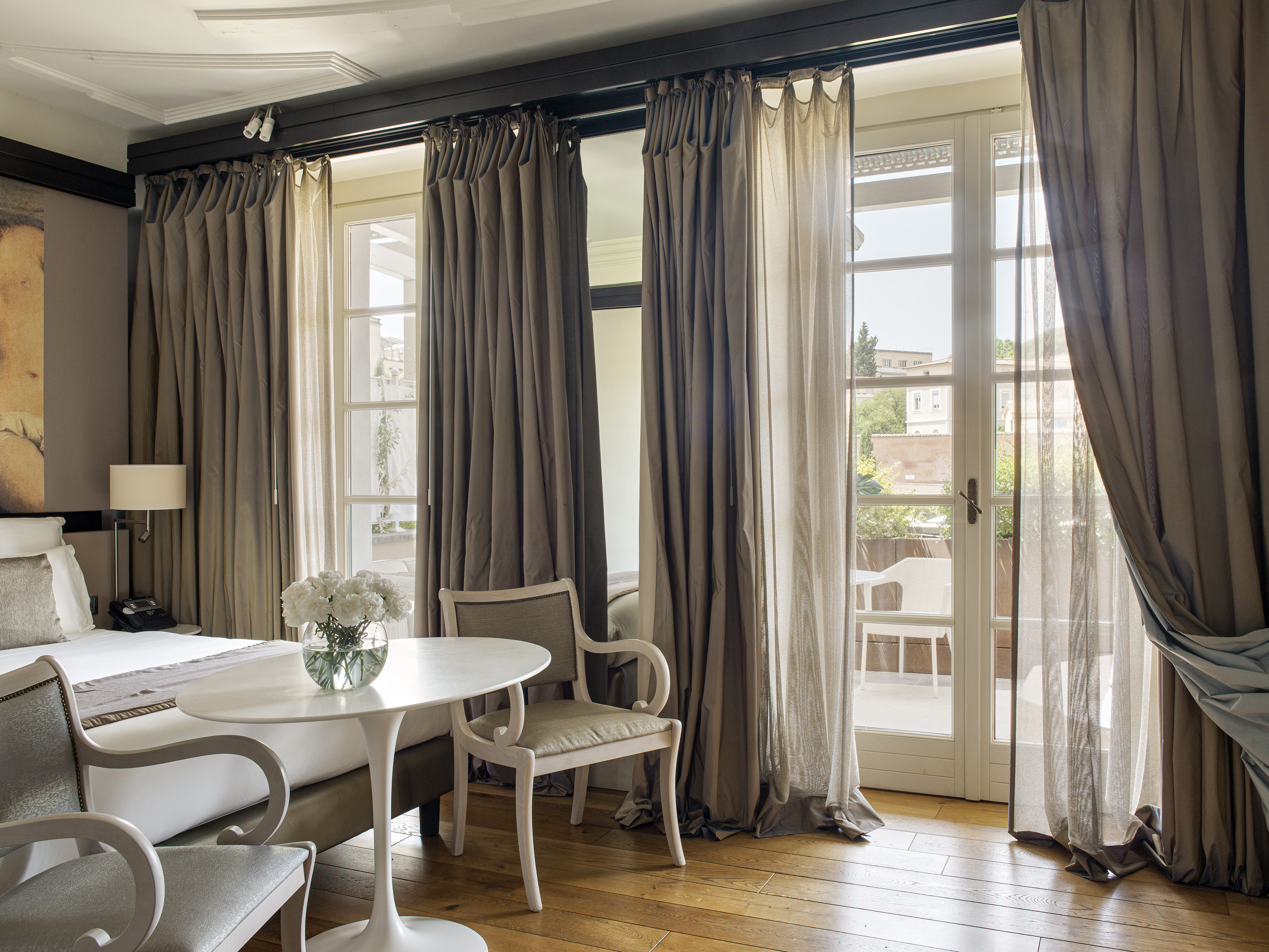 Luxury hotel bedroom with bed, seating, wooden floor, and balcony doors.