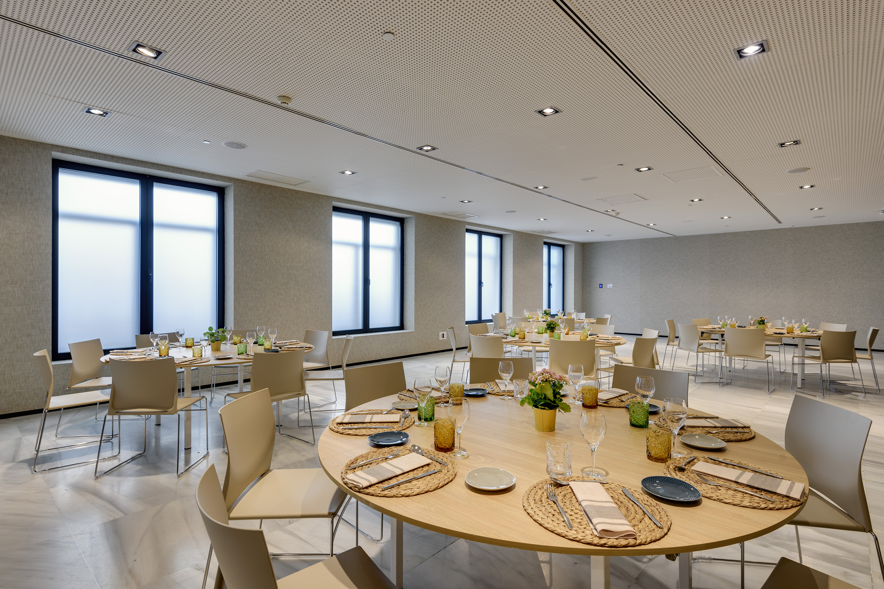 Modern event room, round dining tables set, beige chairs, and frosted windows.