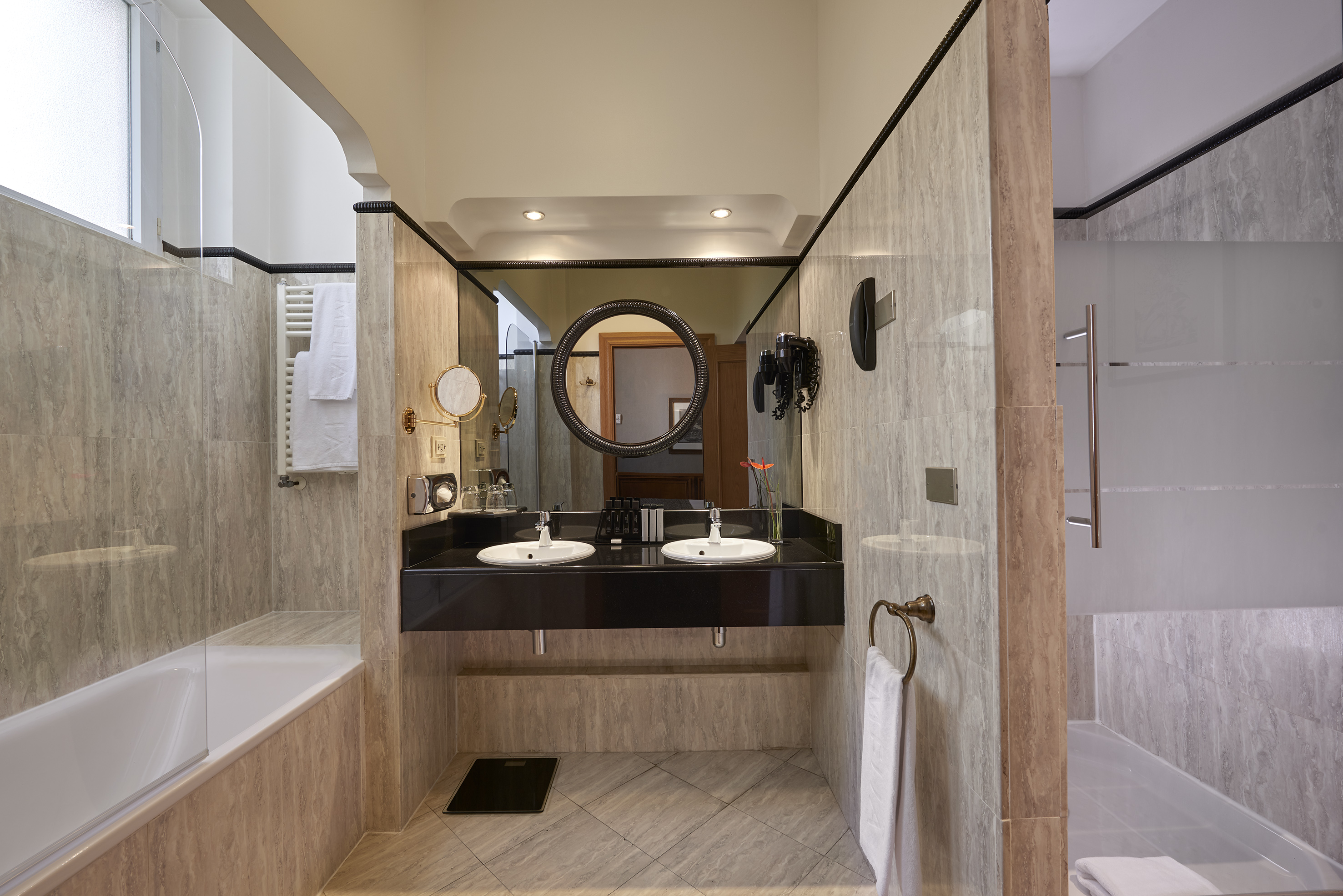 Modern hotel bathroom with dual vanity, large mirror, bathtub, and shower.