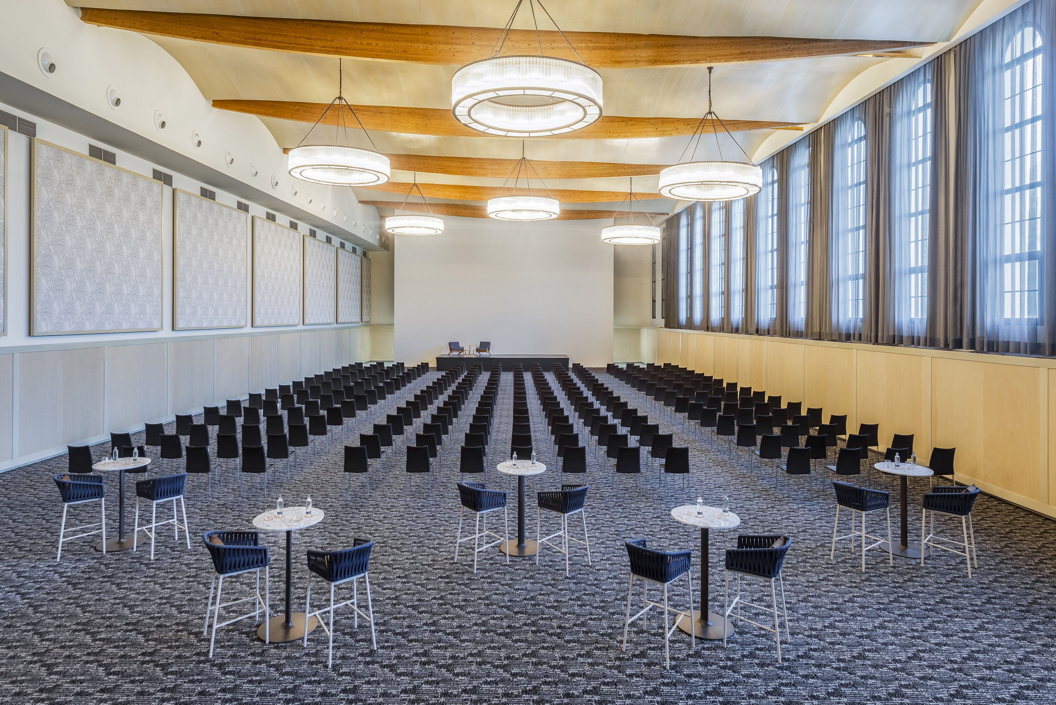 Modern event venue with theater seating, presentation stage, and cocktail tables.