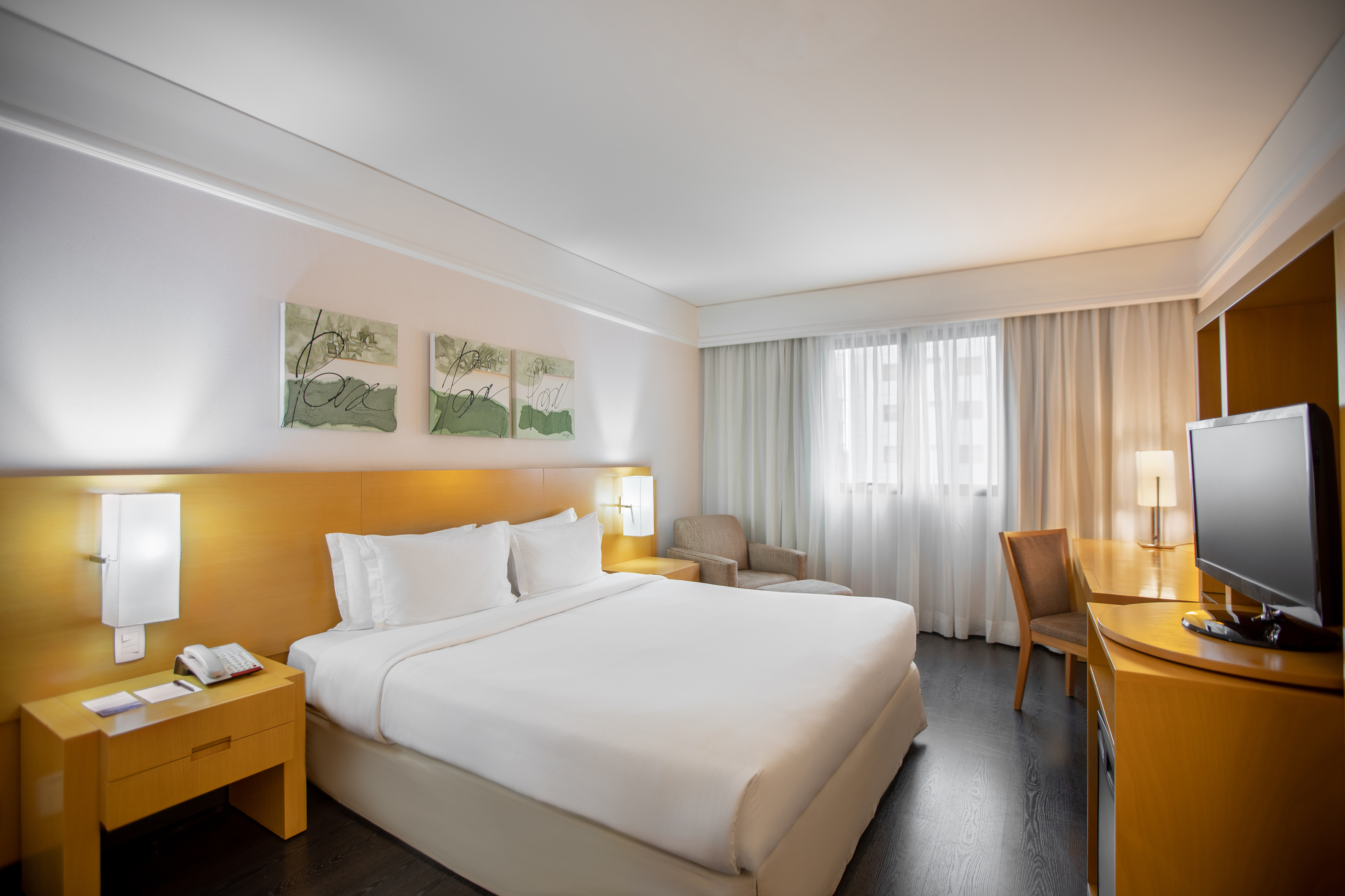 Modern hotel bedroom with king bed, nightstands, desk, TV, and large window.