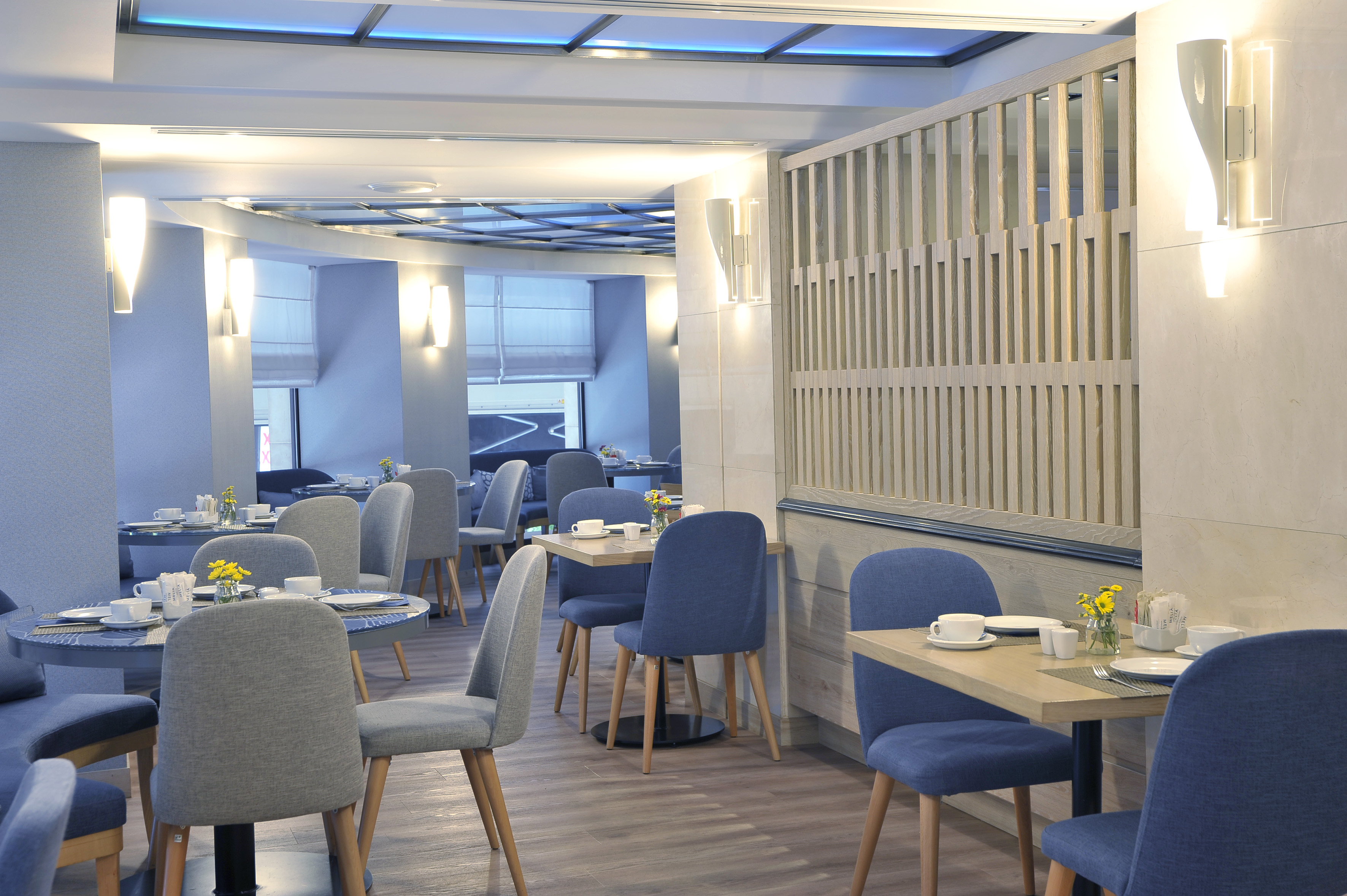Modern hotel restaurant dining area with set tables, blue and grey chairs.