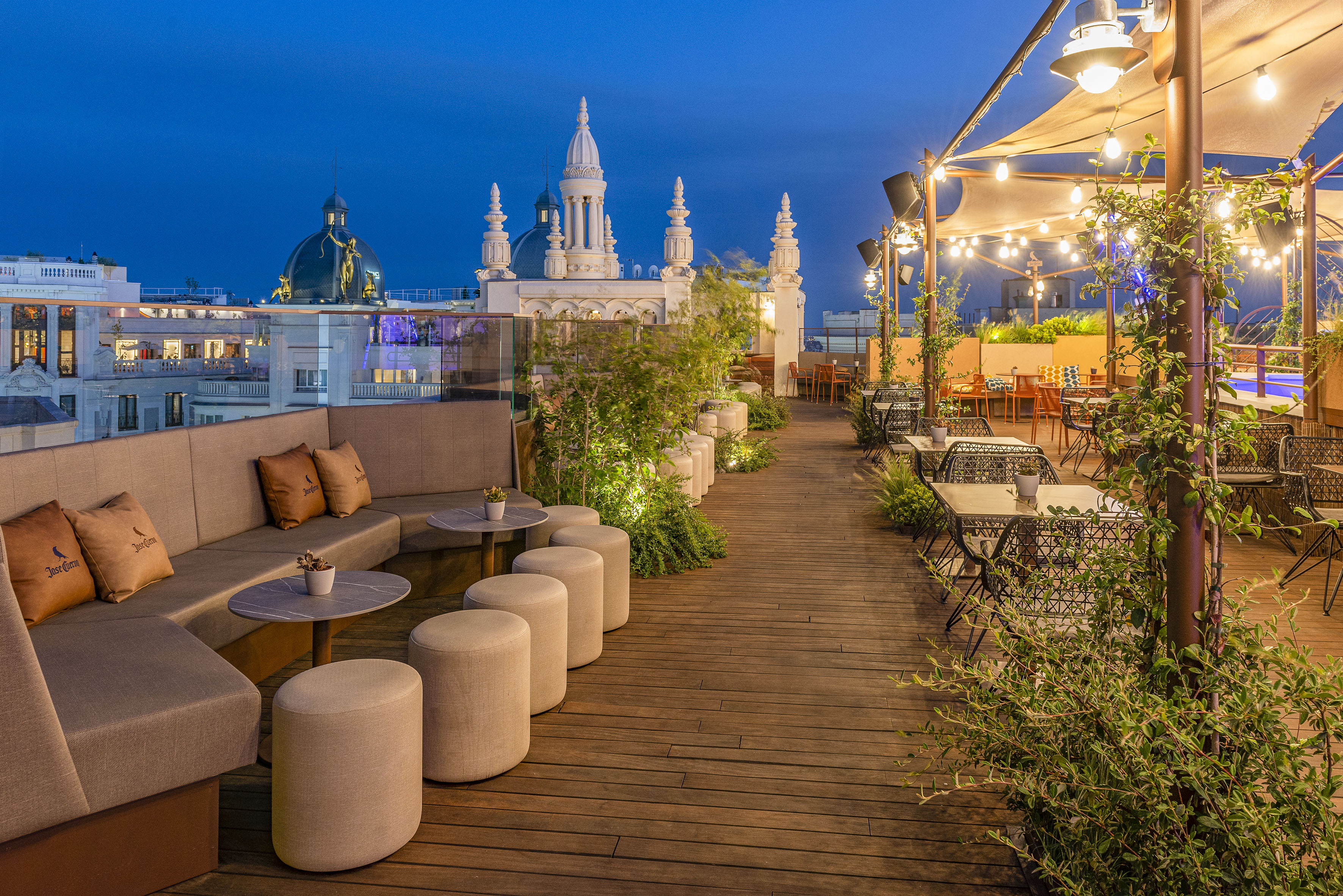 Rooftop bar lounge with outdoor seating, string lights, and city skyline at dusk.