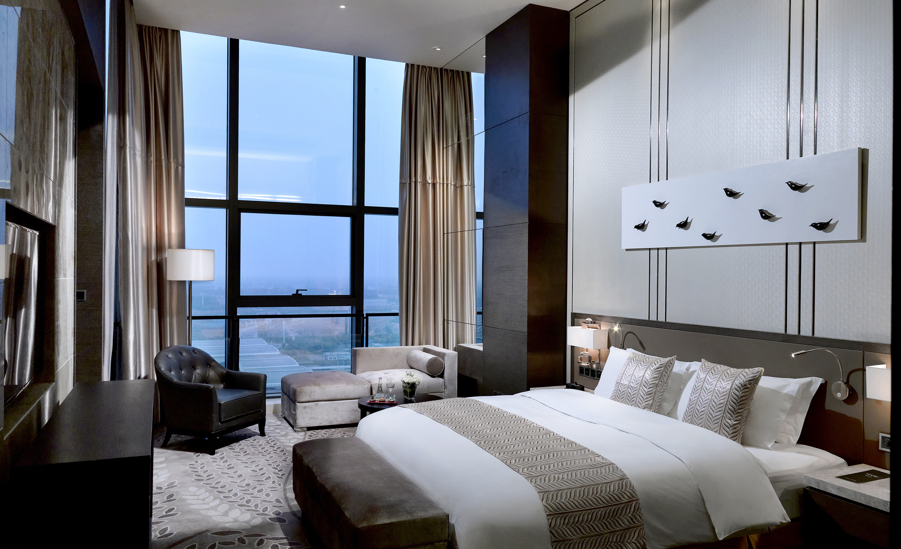 Luxury hotel bedroom with large windows, city view, and elegant king bed.