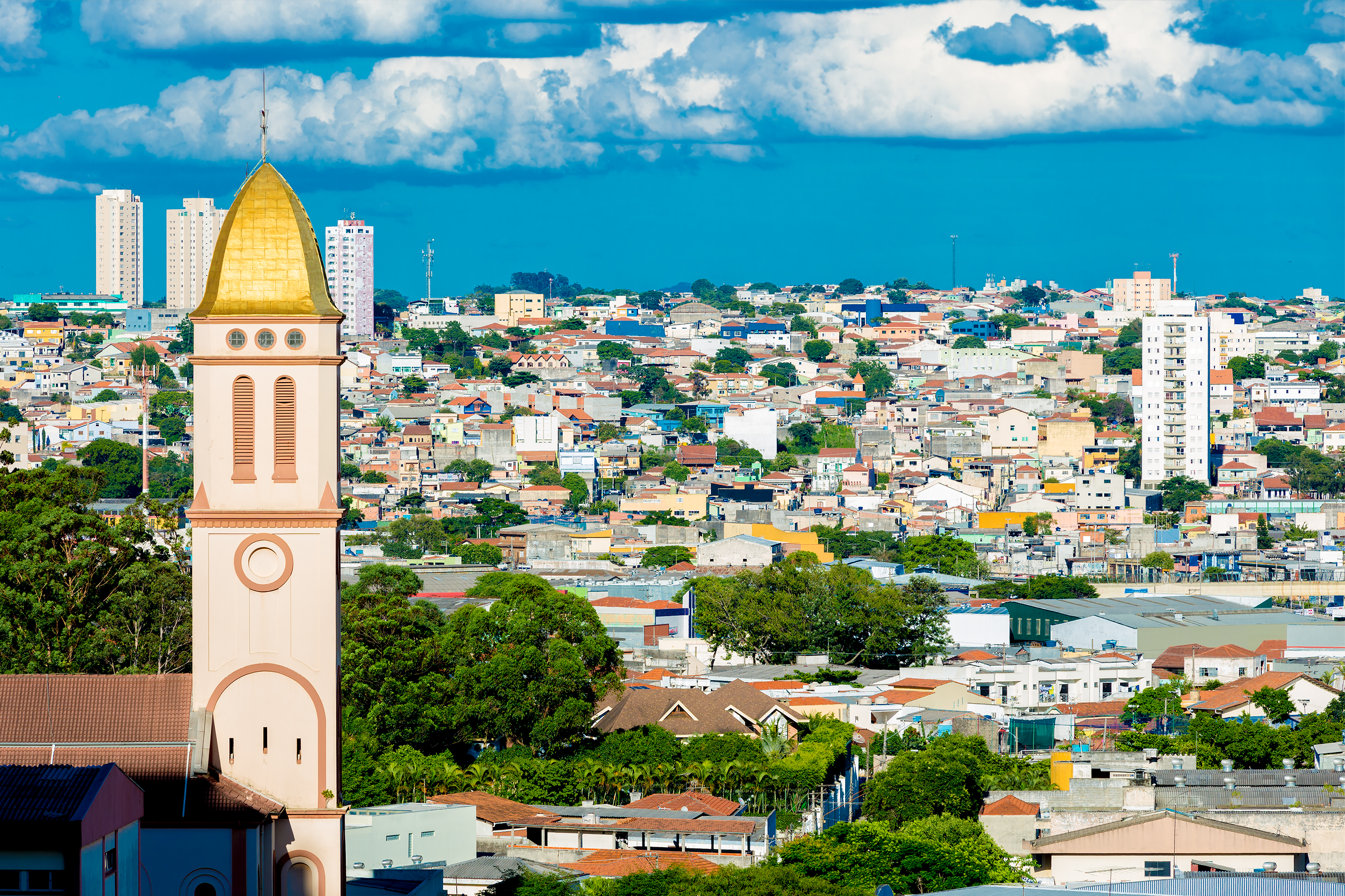 Torre de iglesia con cúpula dorada sobre un paisaje urbano colorido y cielo azul.