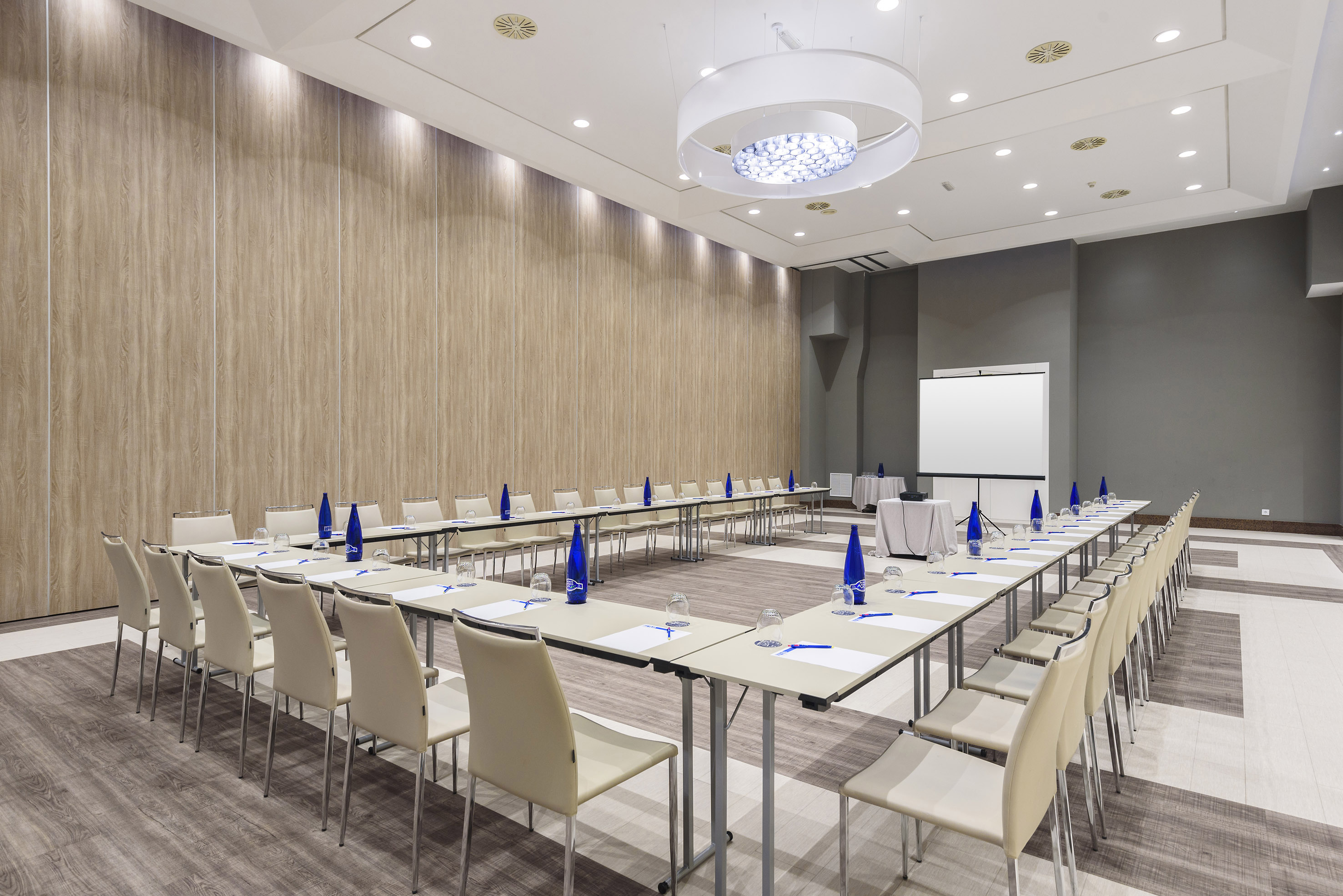 Modern U-shaped meeting room with presentation screen and wood paneling.