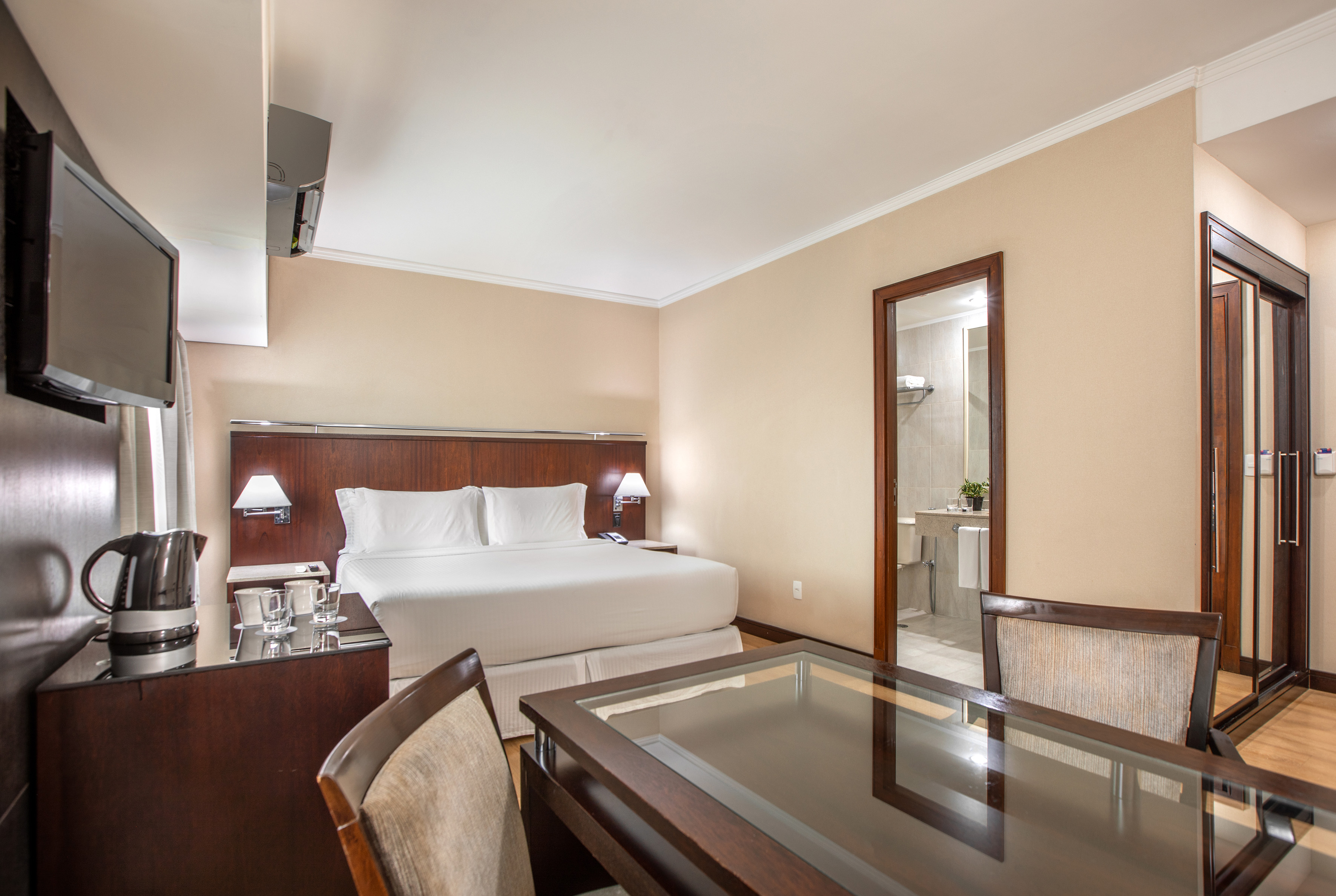 Modern hotel room interior with king bed, desk, TV, and bathroom access.
