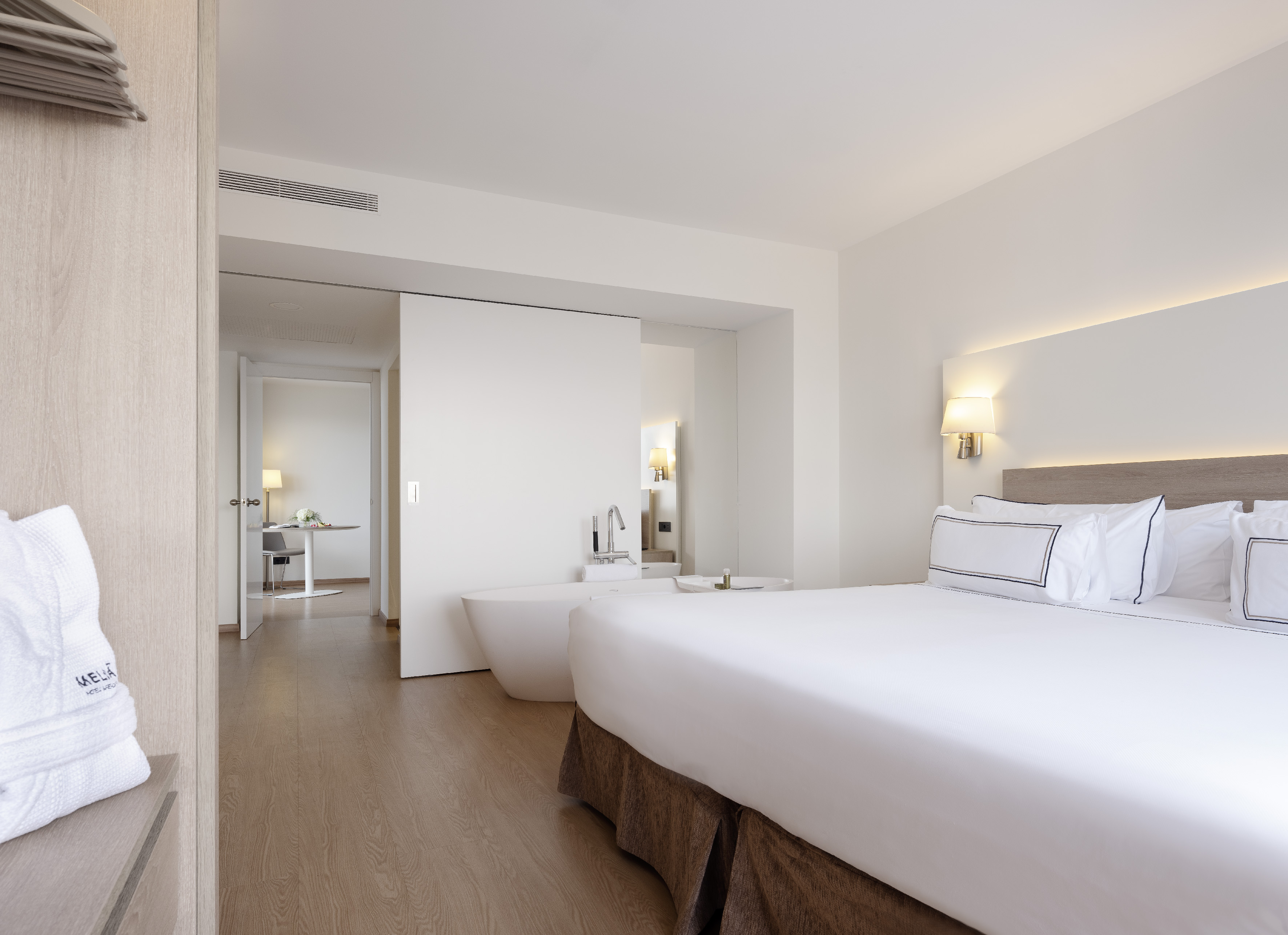 Modern hotel suite with king bed, open-plan bathroom, and bright wooden floors.