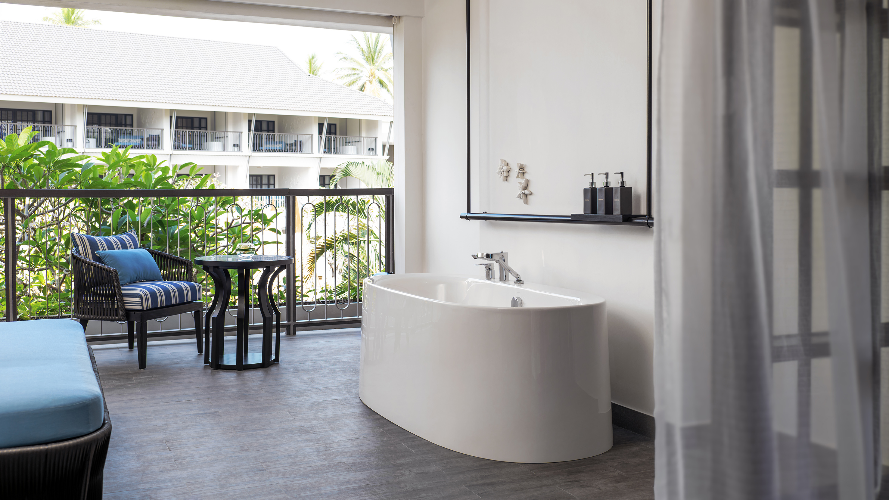 Freestanding bathtub on tropical hotel balcony with resort view.