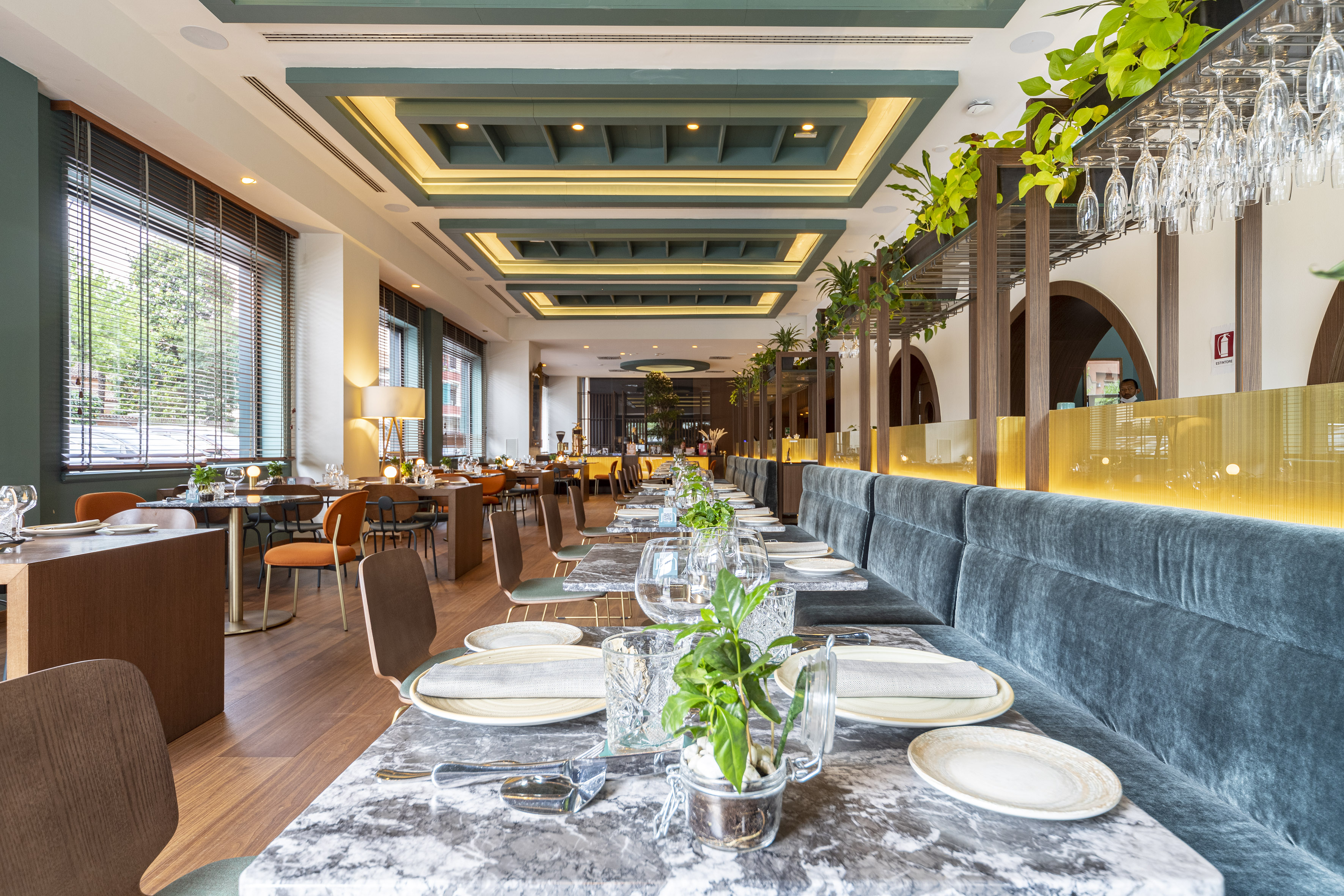 Modern restaurant interior with teal banquettes, marble tables, and green decor.