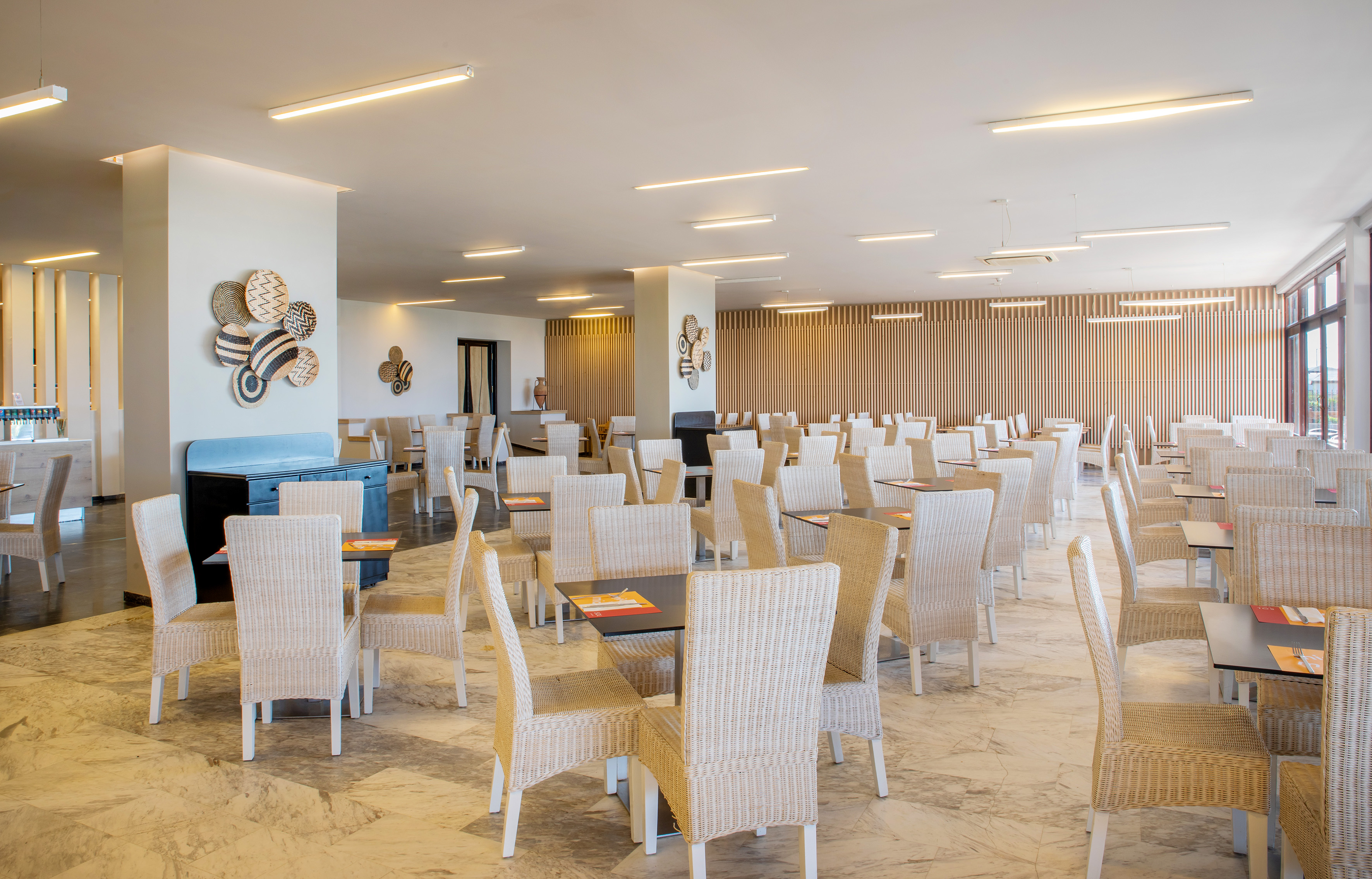 Empty modern hotel dining room with wicker chairs and tables.