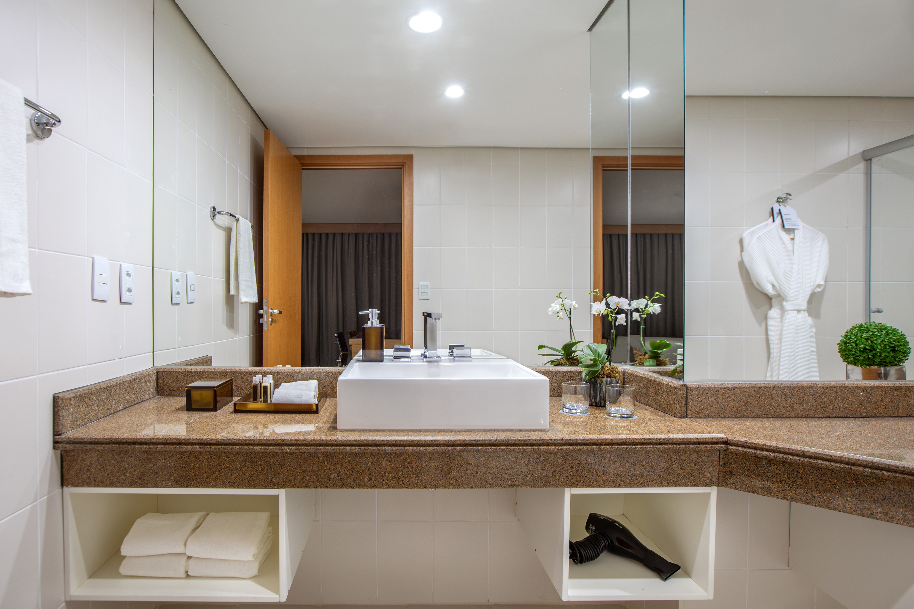 Modern hotel bathroom with granite vanity, vessel sink, and white towels.