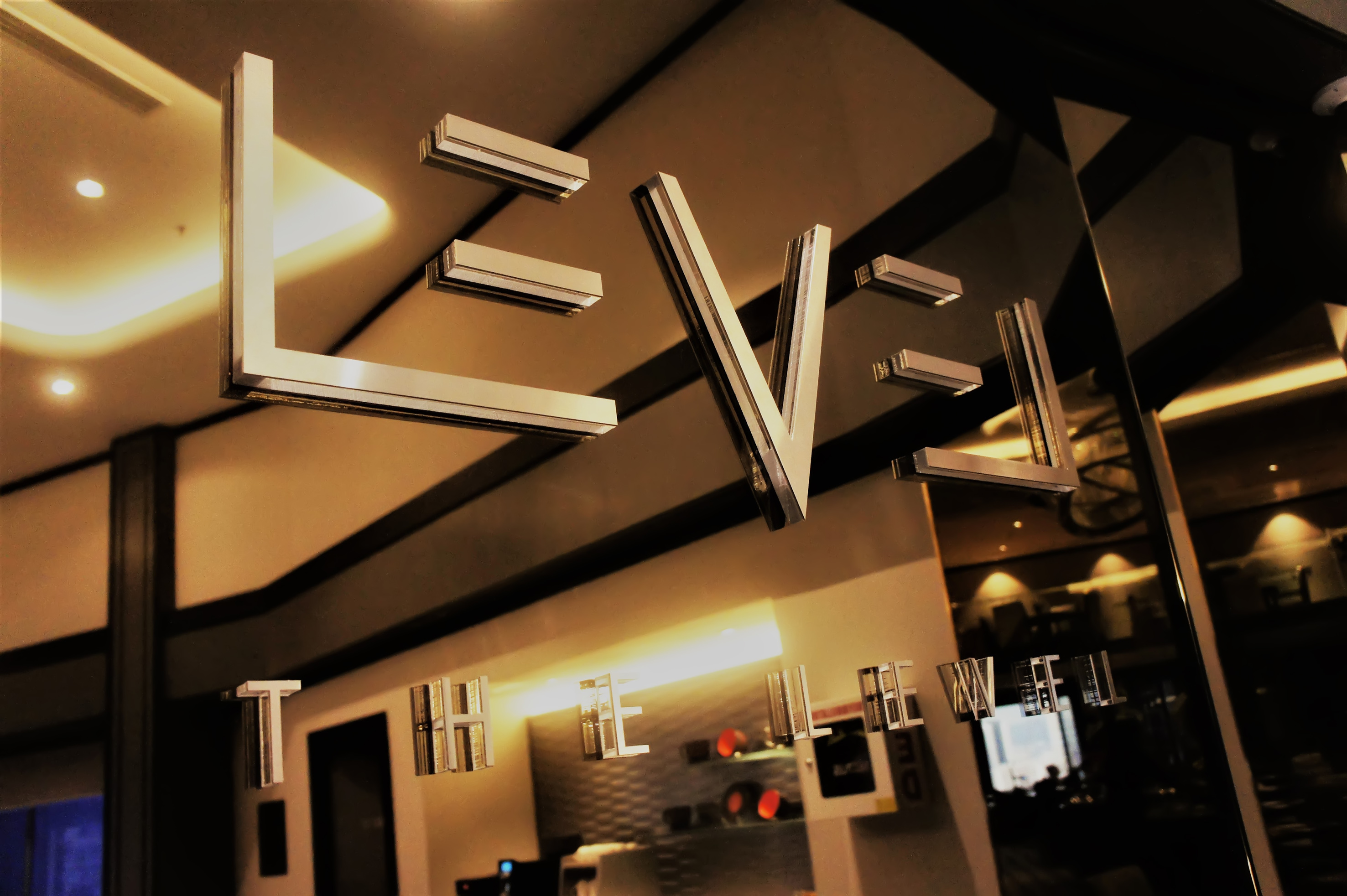 Metallic 3D 'THE LEVEL' sign on reflective surface in modern hotel interior.