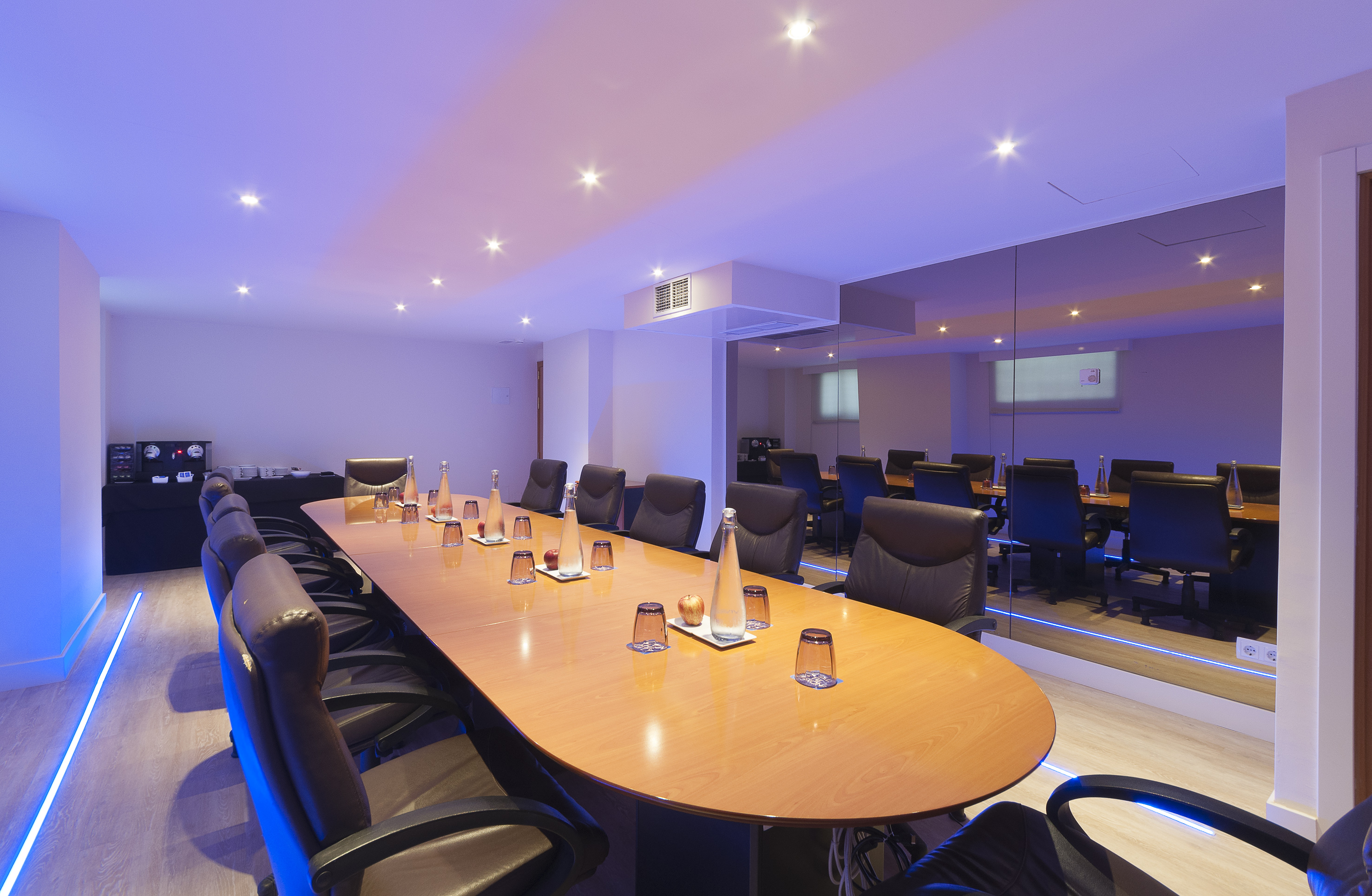 Modern boardroom with oval wooden table, leather chairs, and blue LED lighting.