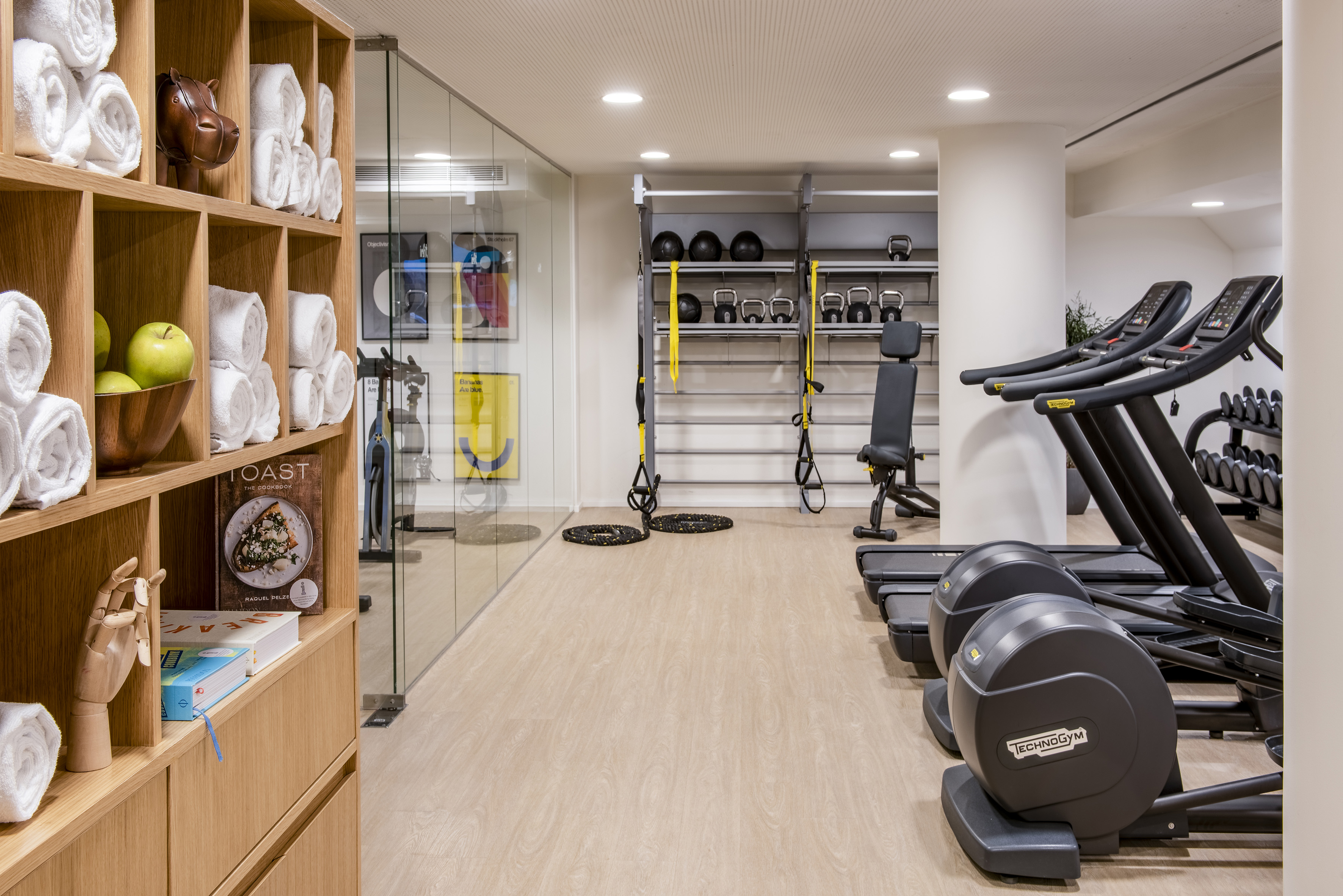 Modern hotel gym with Technogym equipment, treadmills, weights, and towel station.
