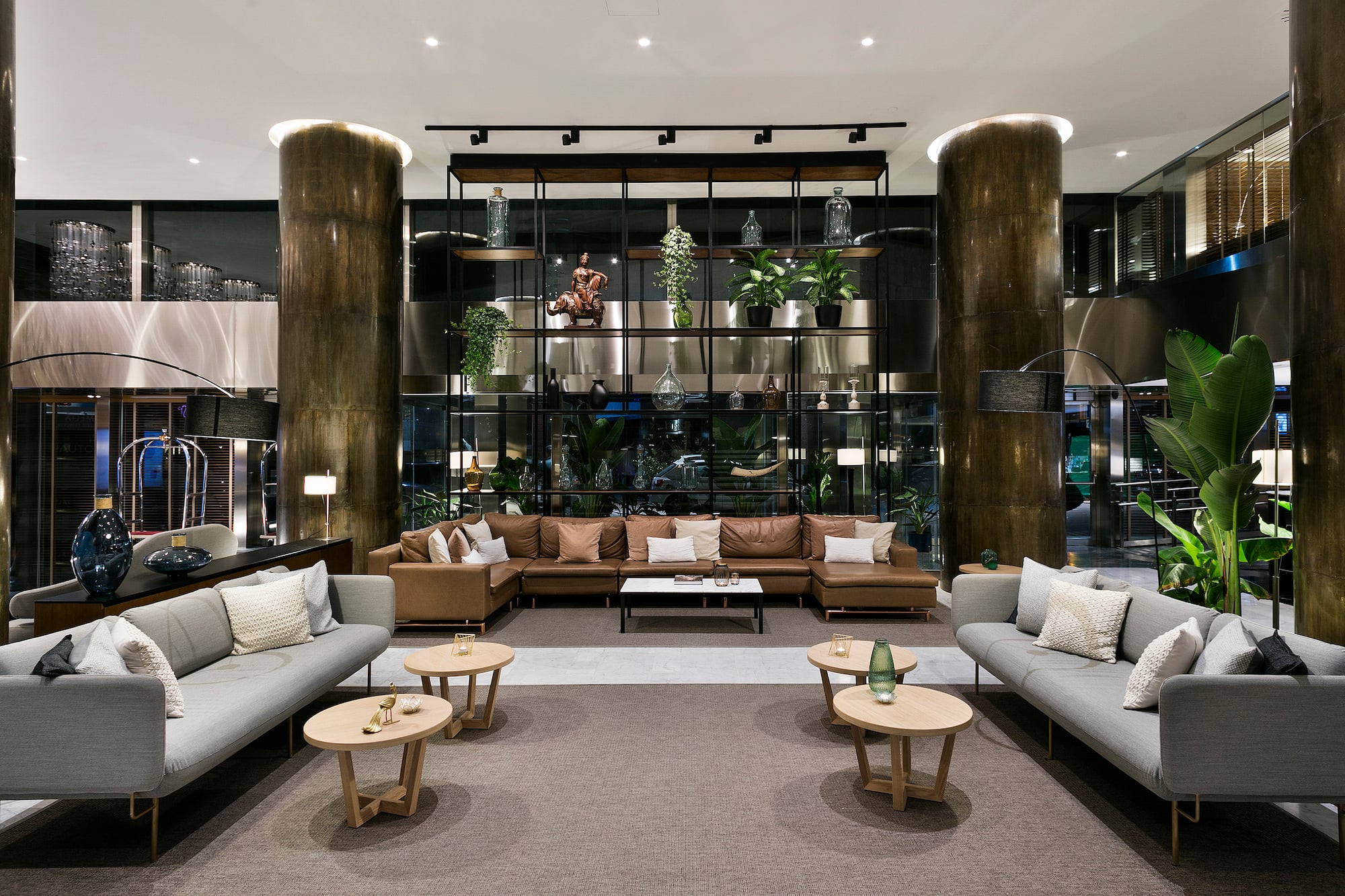 Elegant hotel lounge featuring modern sofas, decorative shelving, and lush plants.