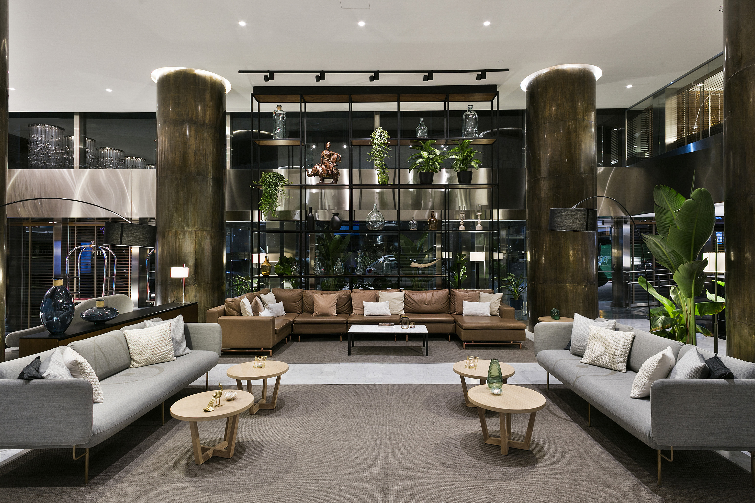 Elegant hotel lounge featuring modern sofas, decorative shelving, and lush plants.