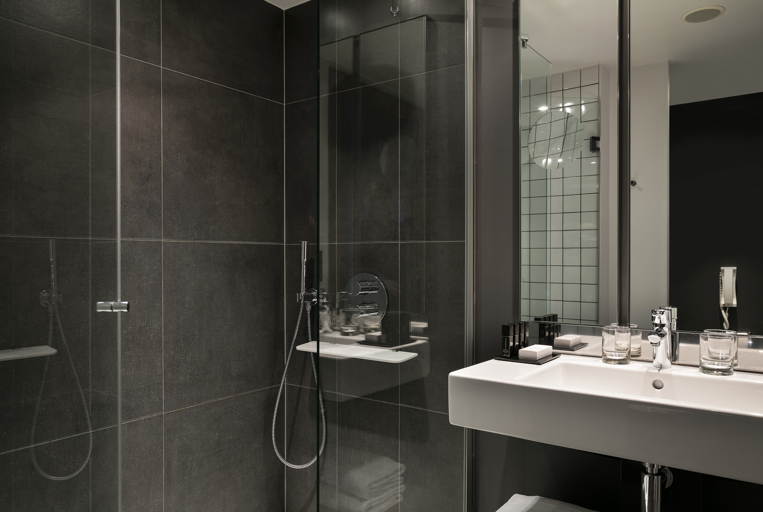 Modern bathroom with dark gray tiled shower, glass enclosure, and white sink vanity.