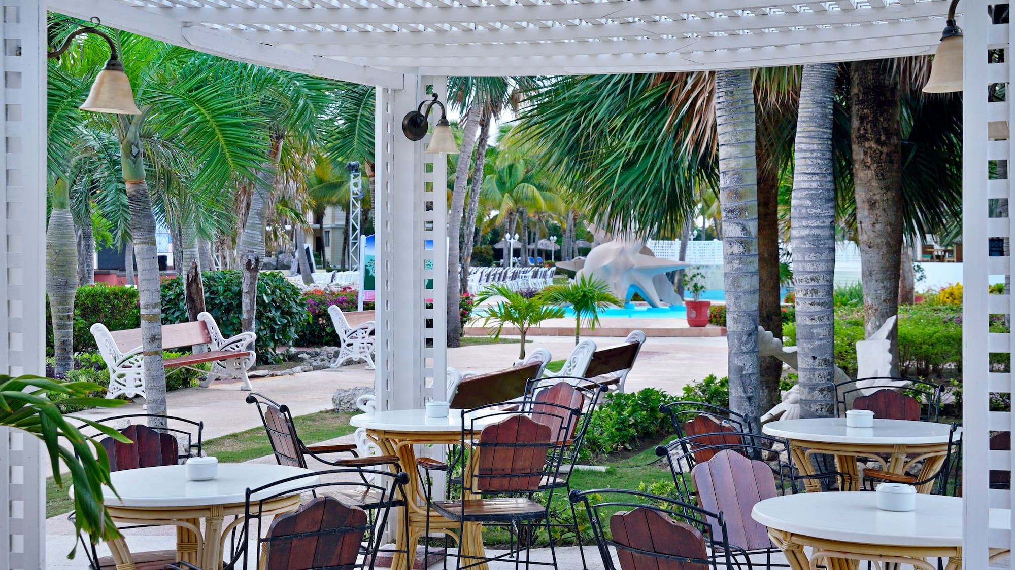 a white pergola with tables and chairs under a white arbor