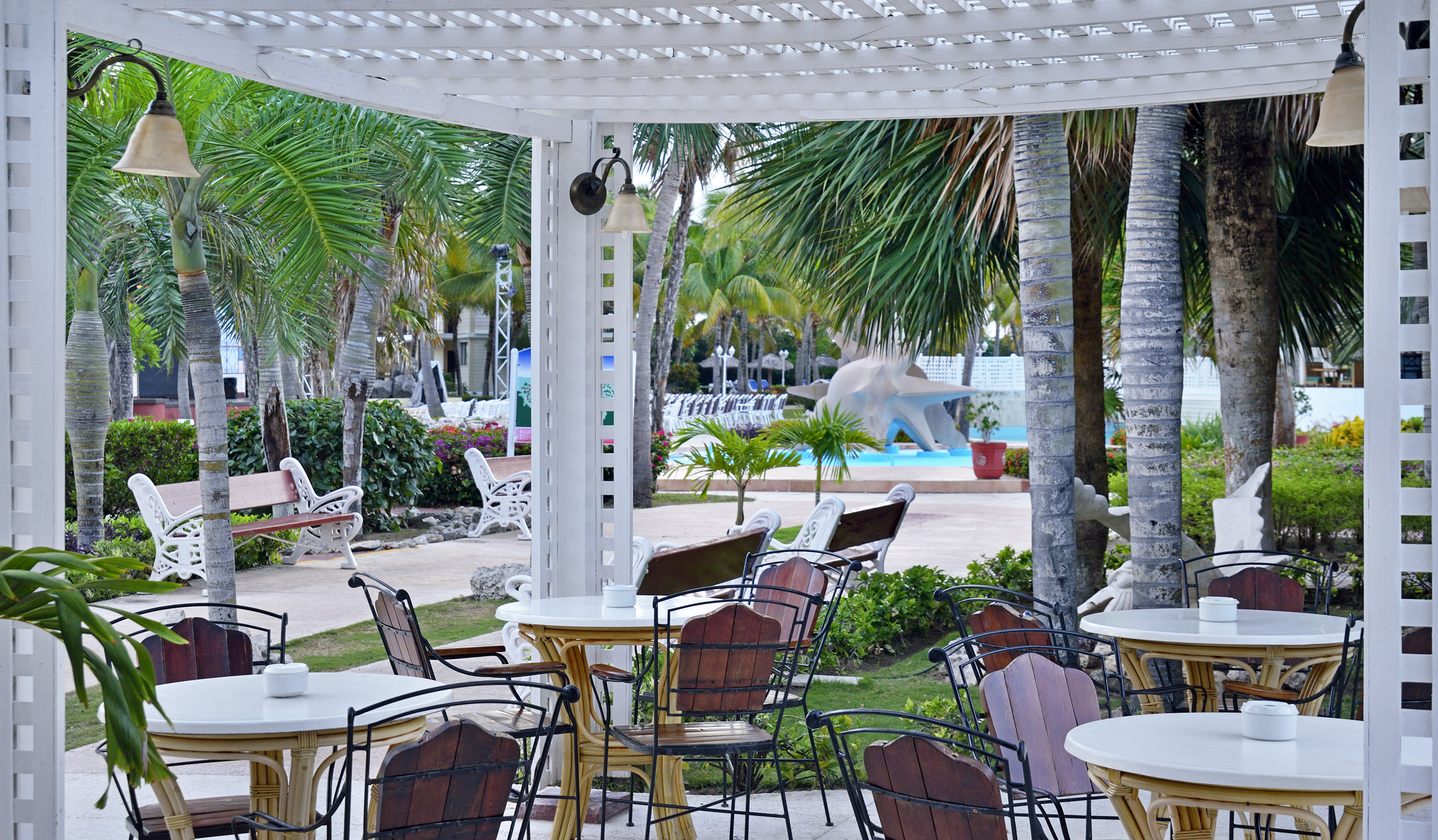 a white pergola with tables and chairs under a white arbor
