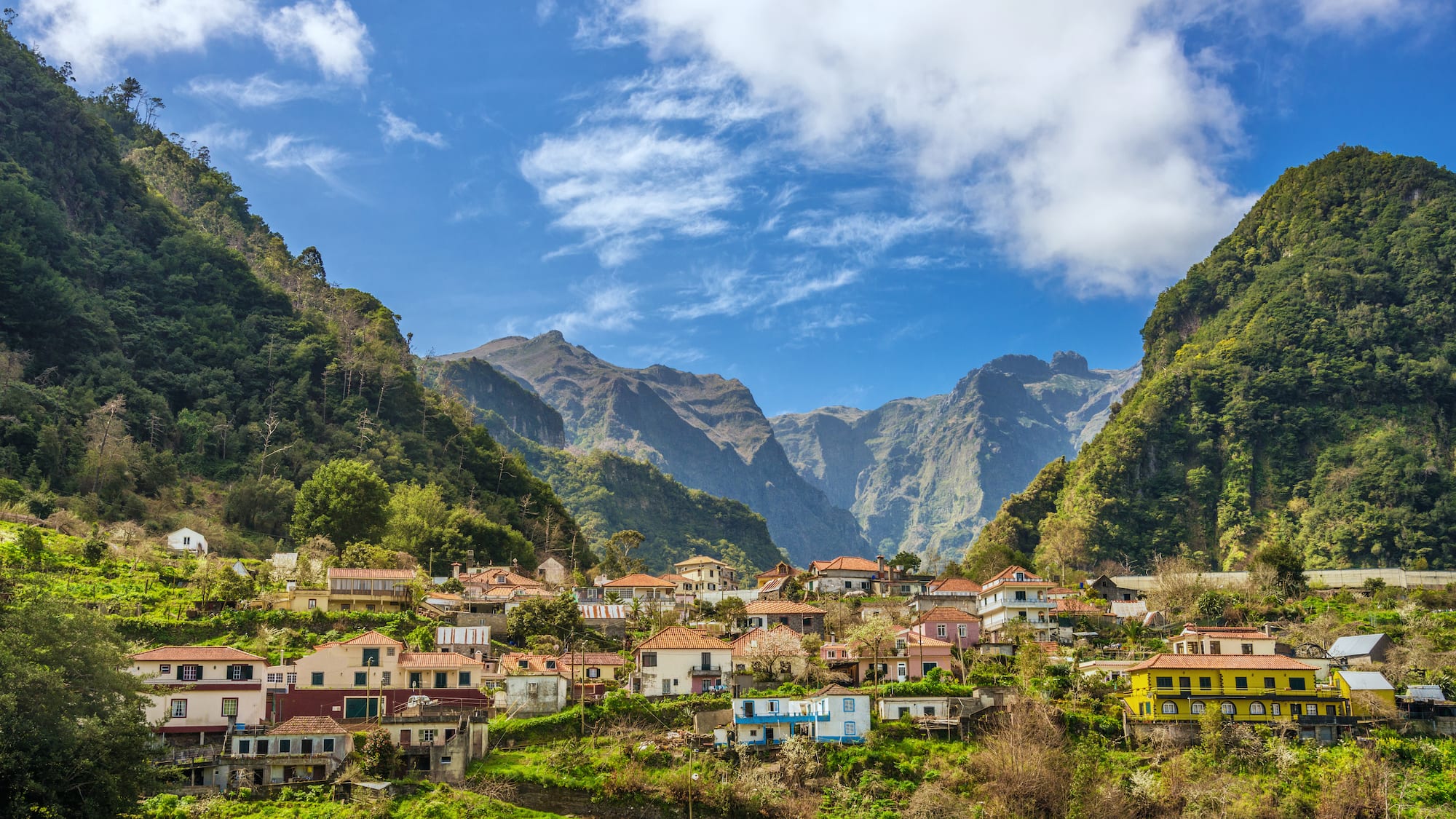 a group of houses in a valley with mountains and blue sky
