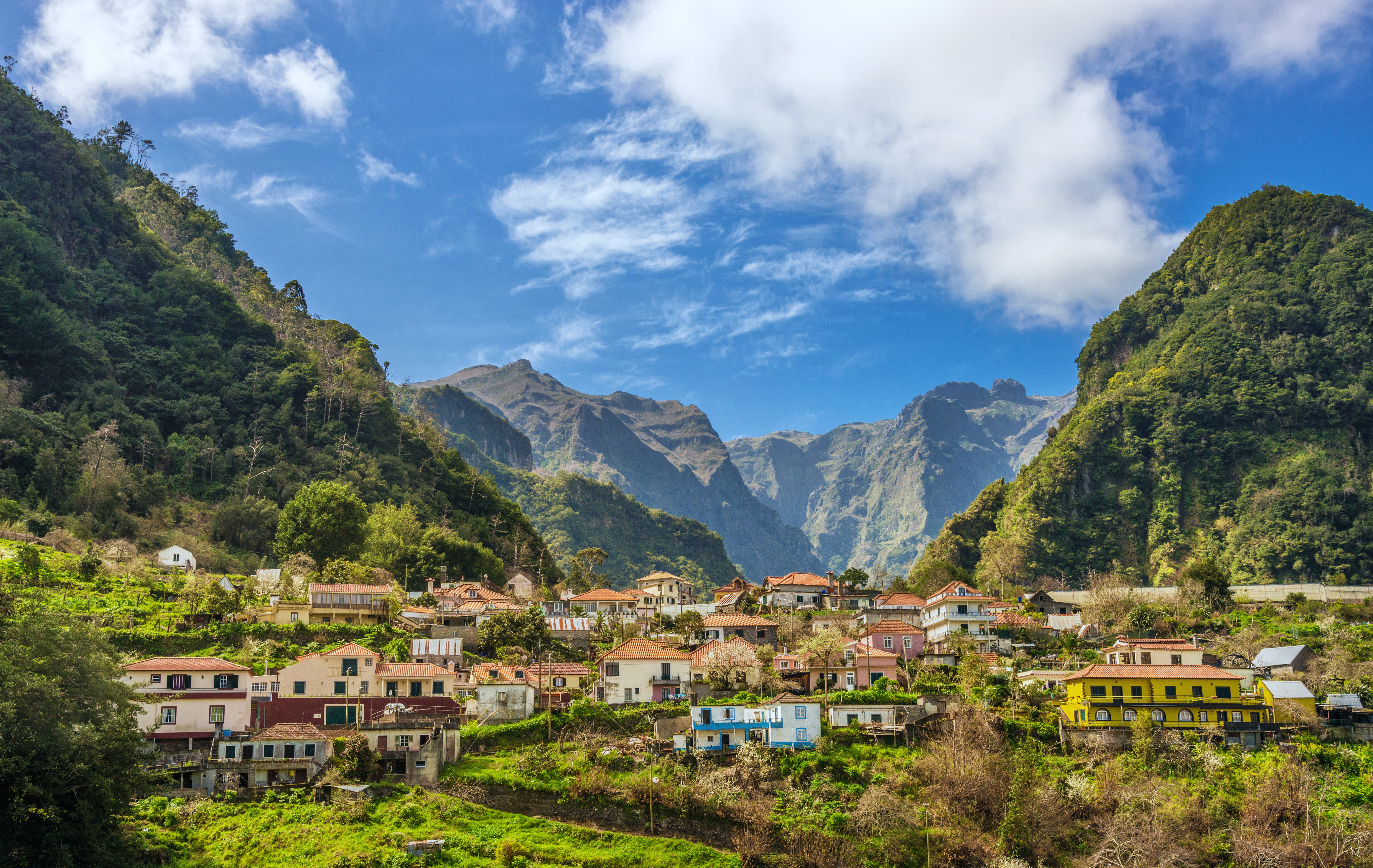 a group of houses in a valley with mountains and blue sky