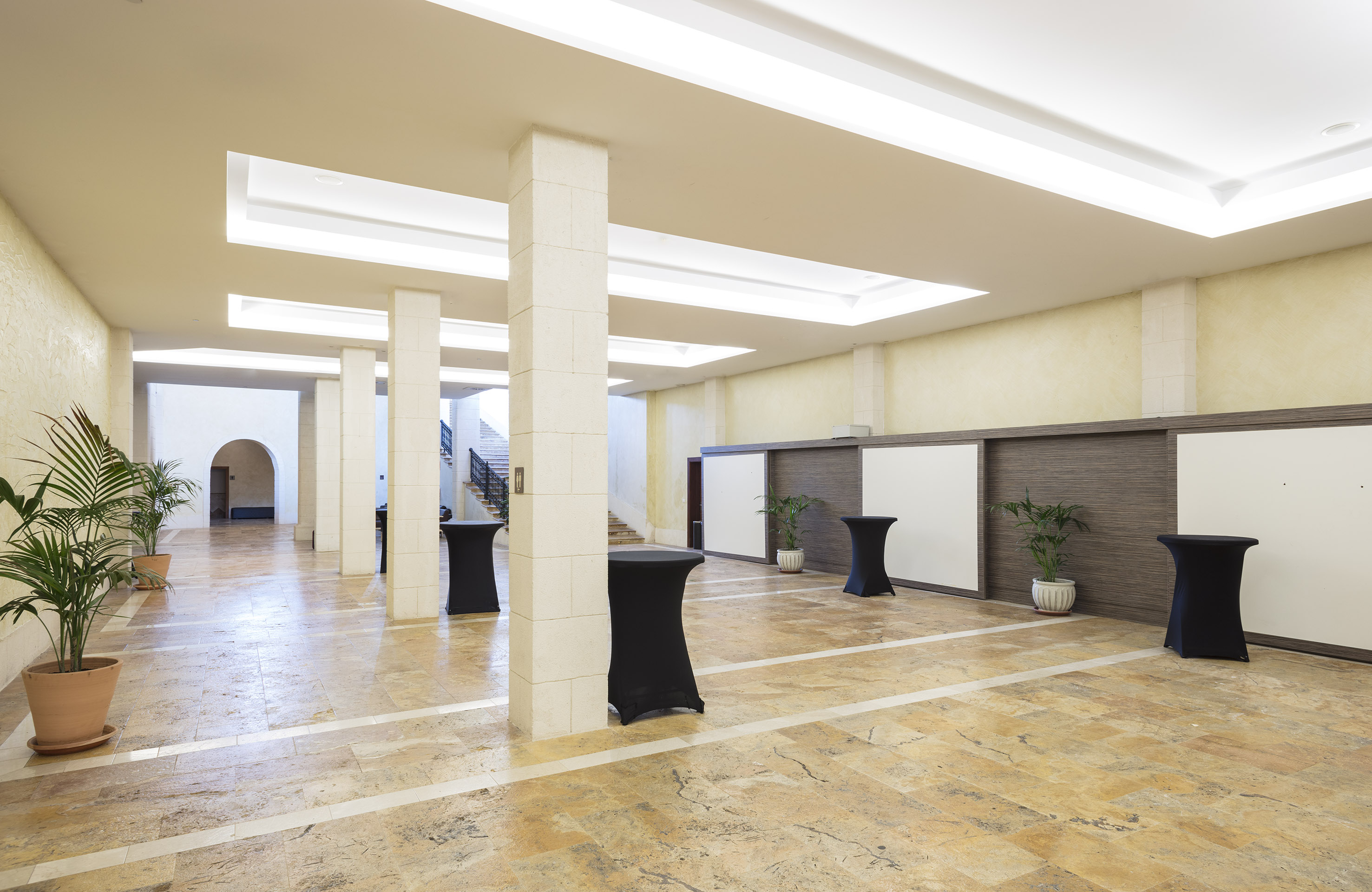 Bright hotel lobby with tiled floor, columns, recessed lighting, and event tables.