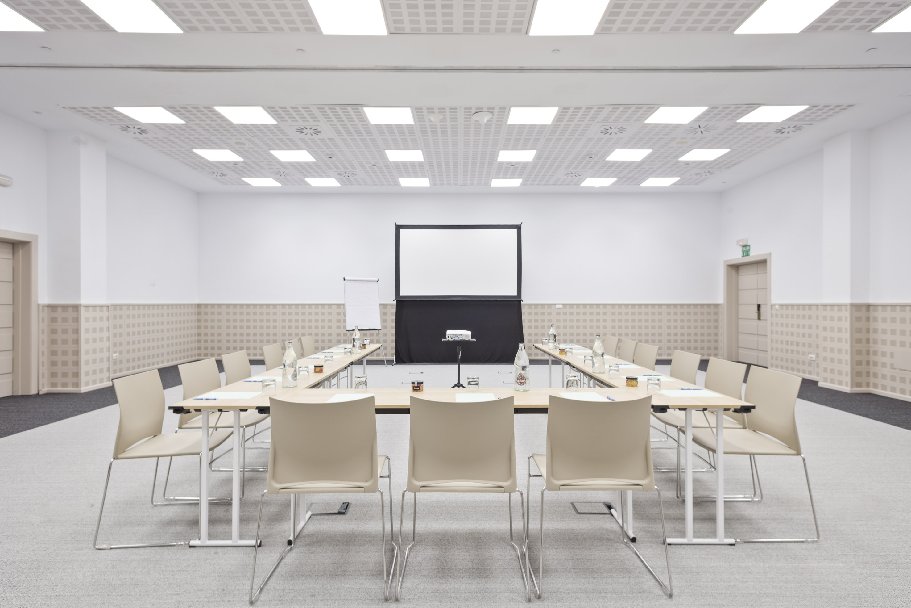 Bright, empty conference room with U-shaped table setup and projector screen.
