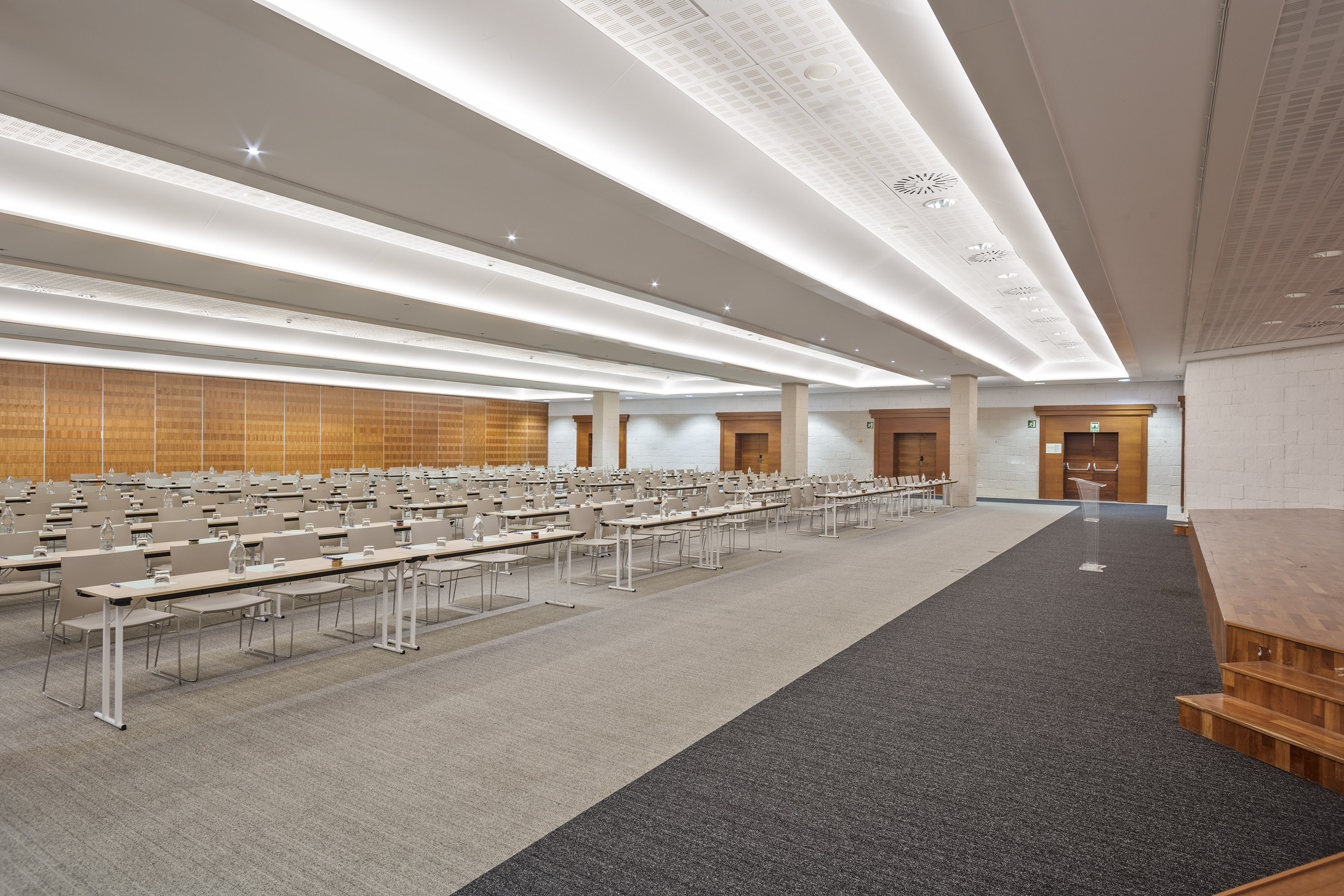 Modern conference room with rows of tables, chairs, and a stage, ready for events.