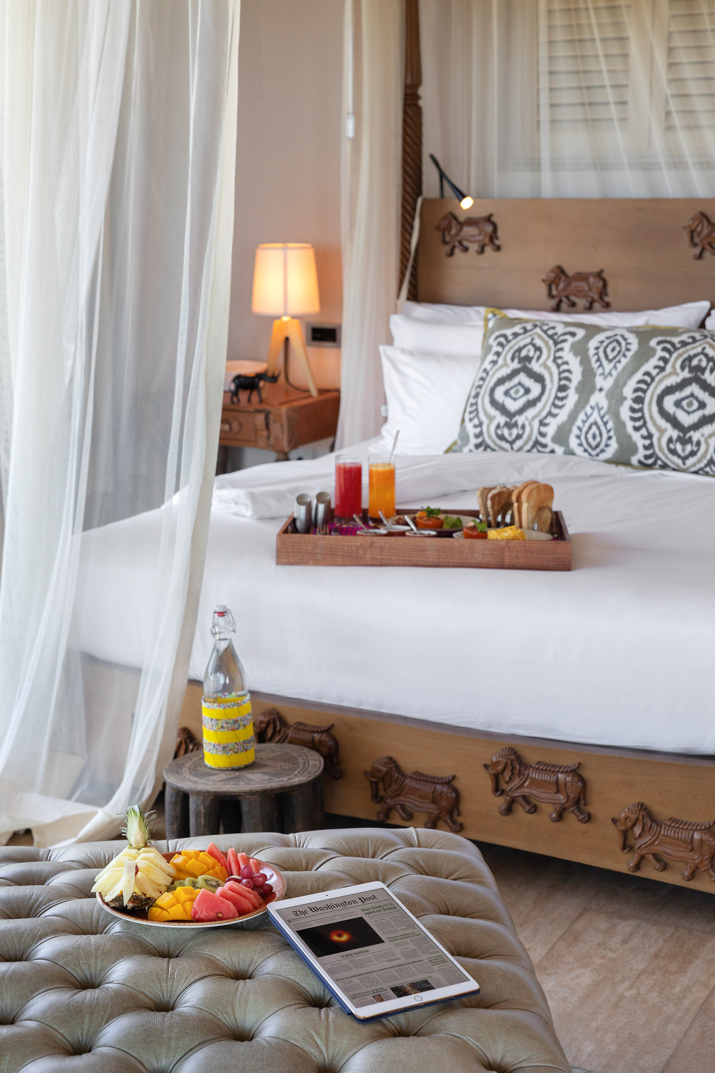 Breakfast in bed in a luxury bedroom suite with fresh fruit and tablet.