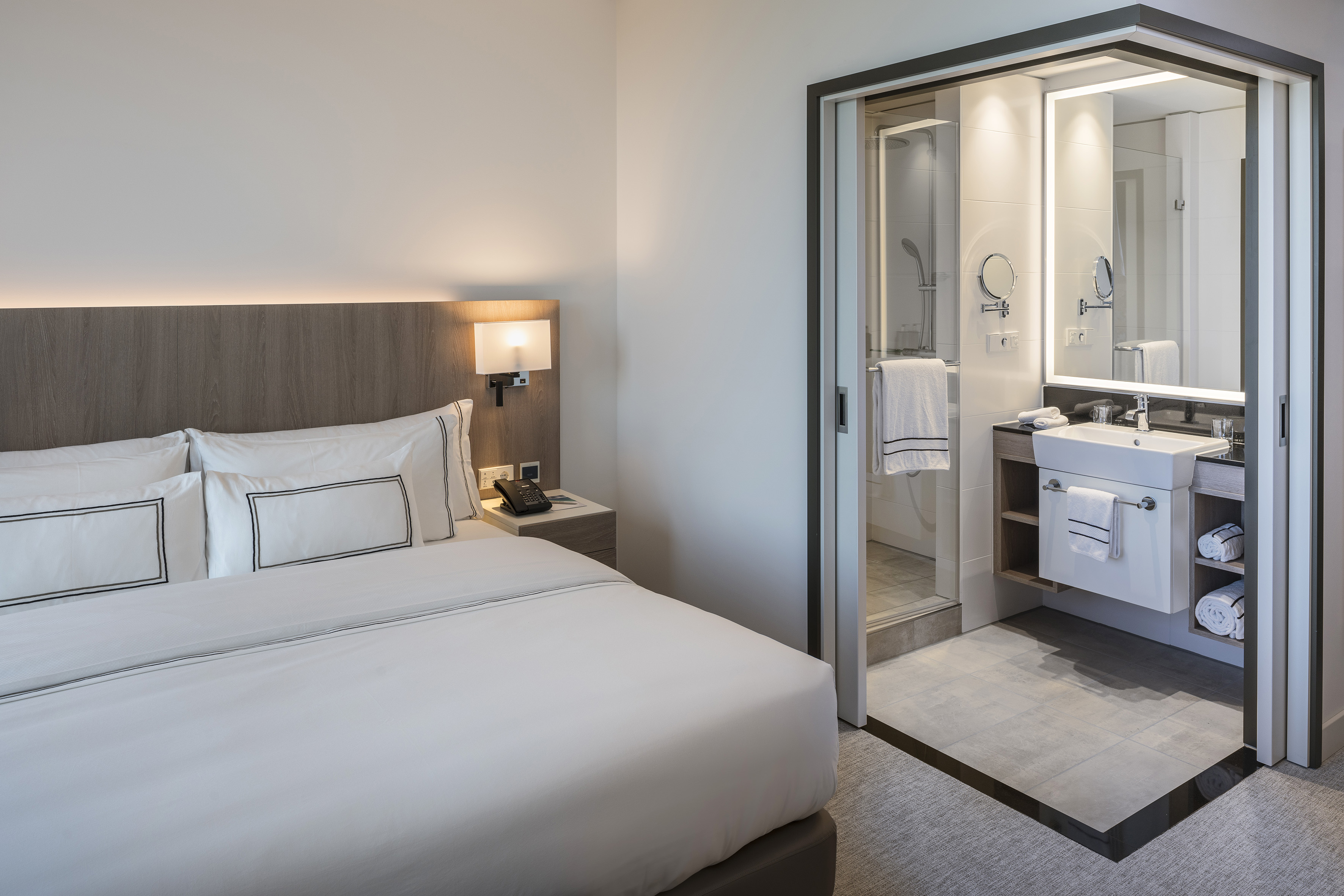 Contemporary hotel bedroom with white bedding and en-suite bathroom.