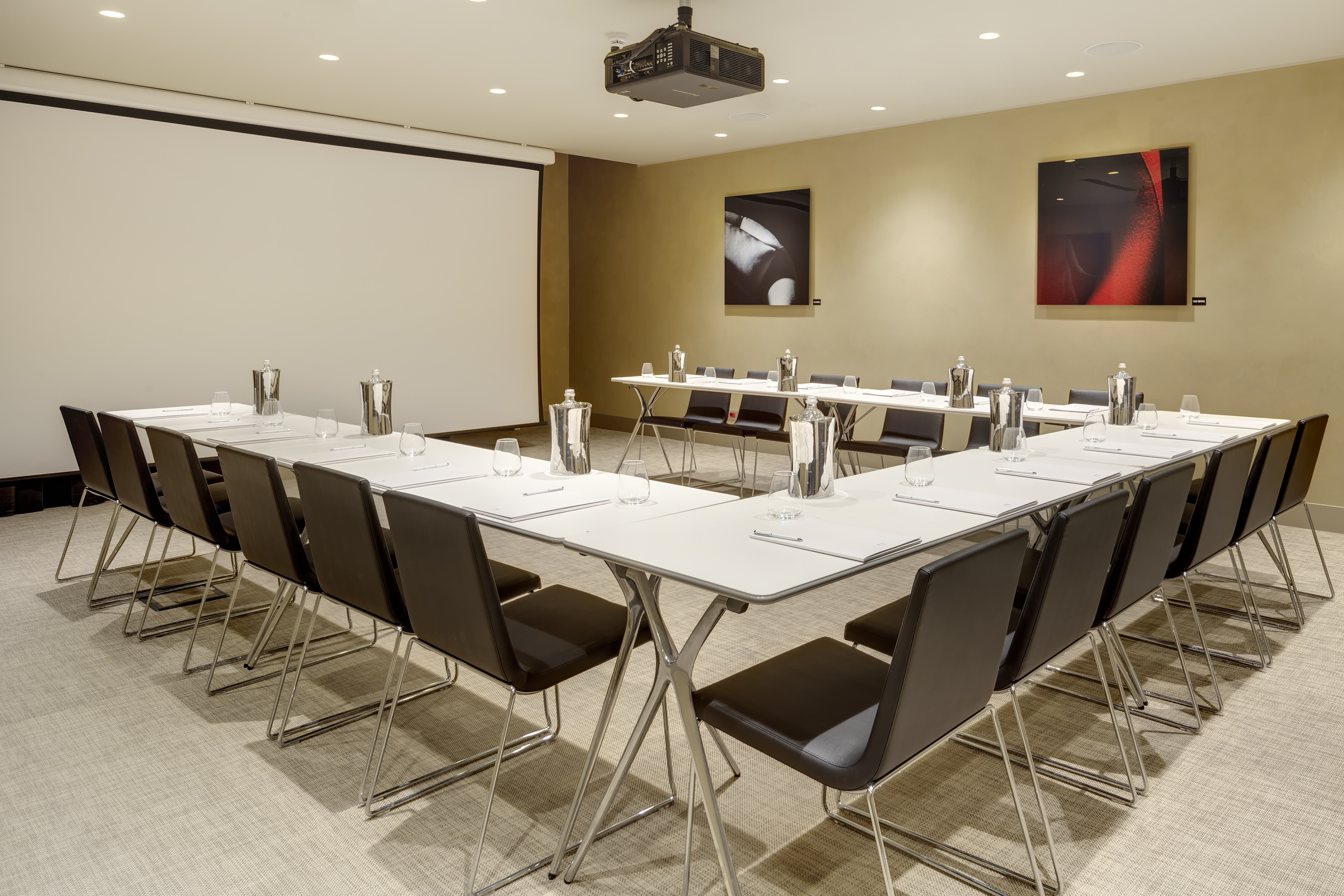 U-shaped conference room with projector screen, modern tables, and black chairs.
