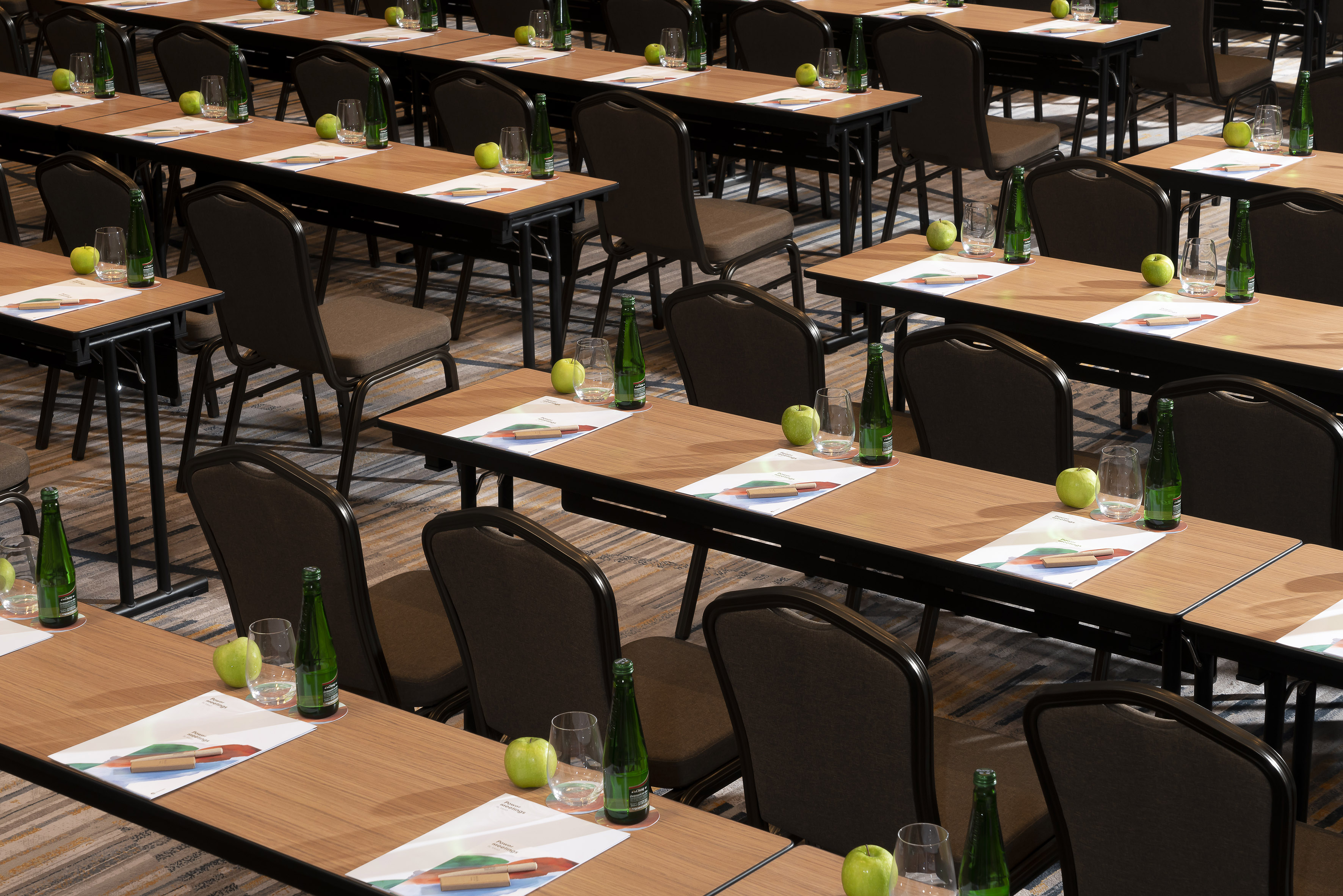 Rows of conference tables with chairs, water bottles, apples, and documents.