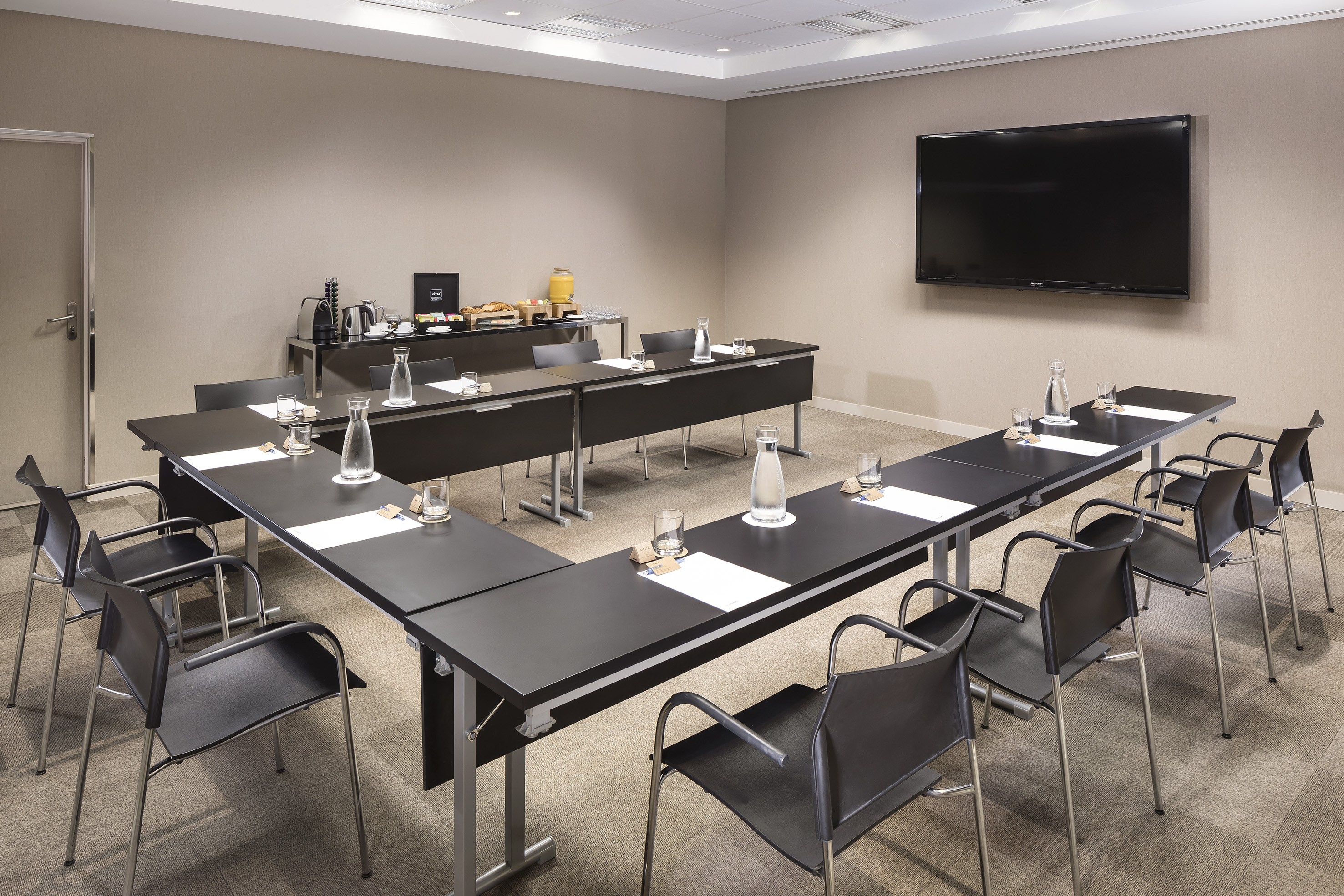 Modern meeting room with U-shaped table, presentation screen, and refreshments.