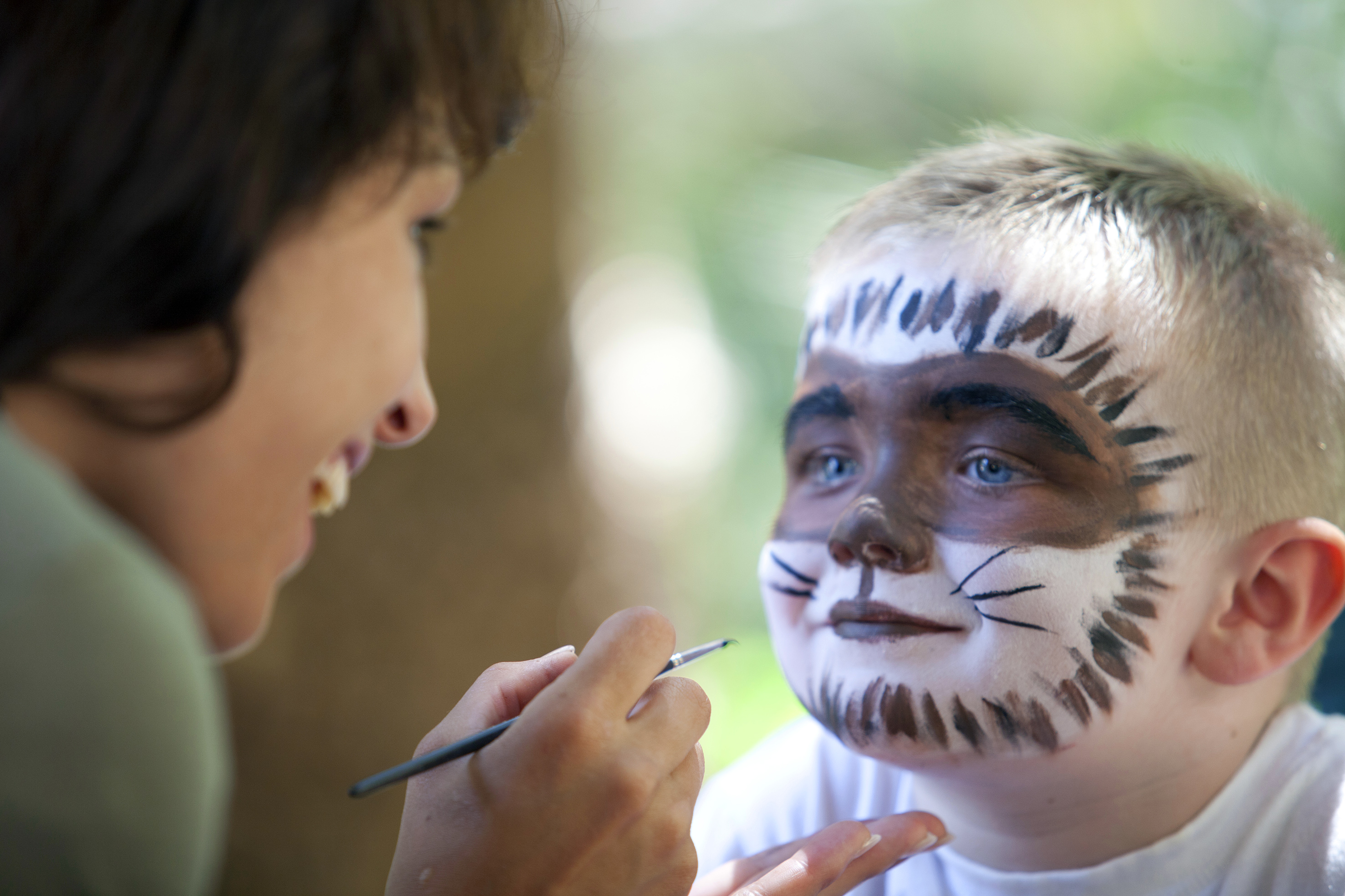 Adult applies brown and white cat face paint to a young boy's face.