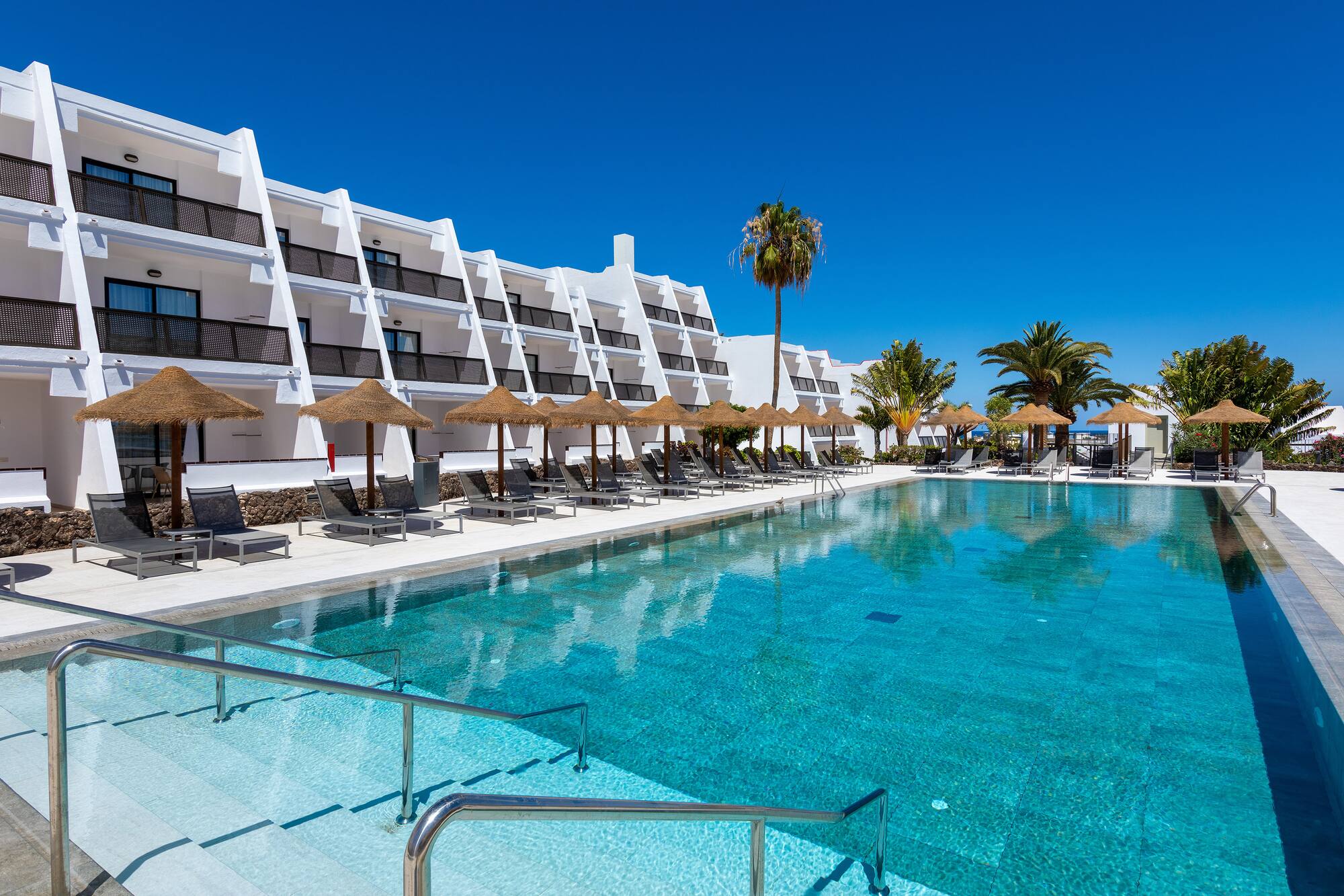 a pool with umbrellas and chairs in front of a building