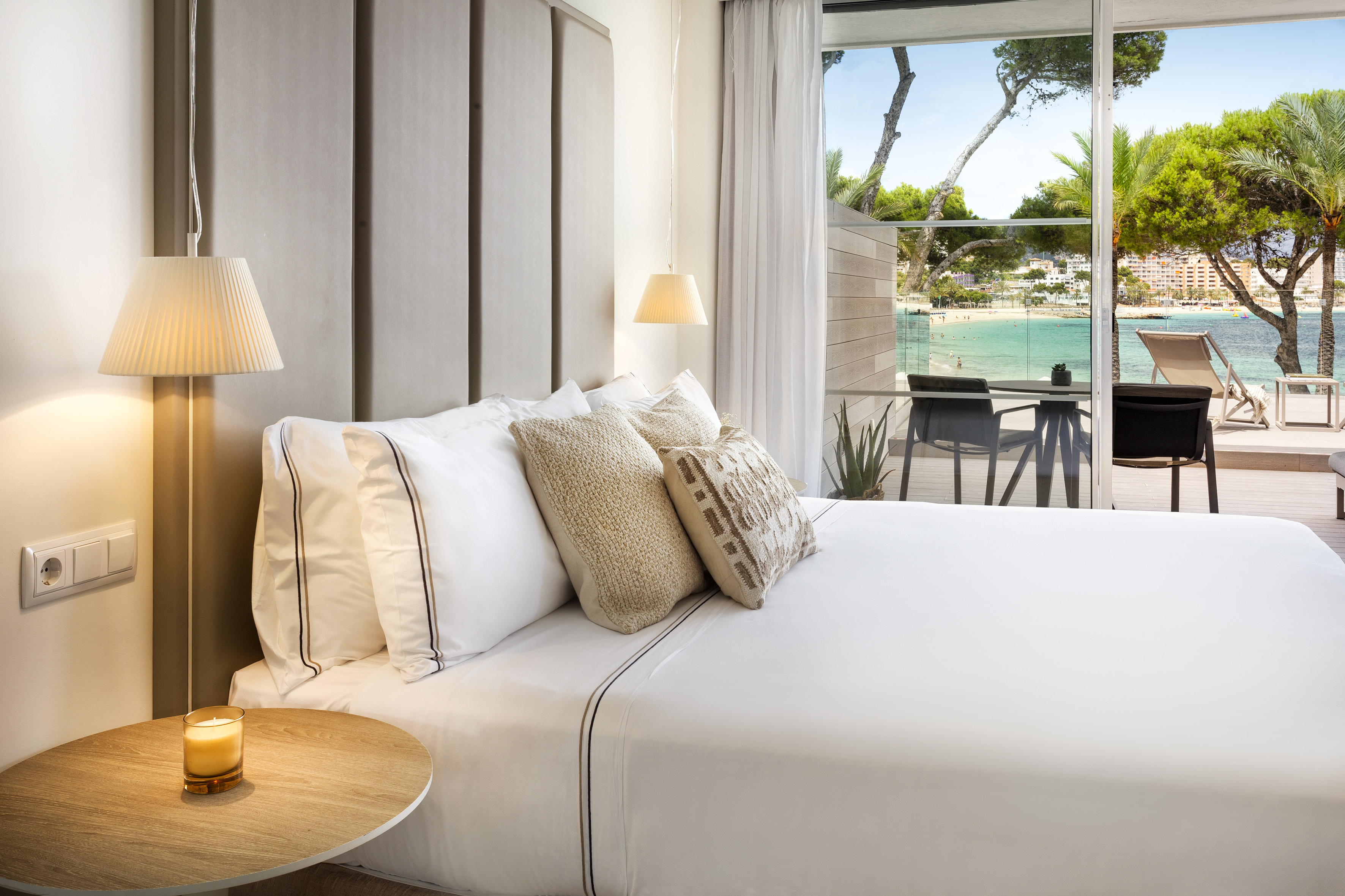 Modern hotel bedroom with bed, nightstand, and balcony overlooking beach ocean.