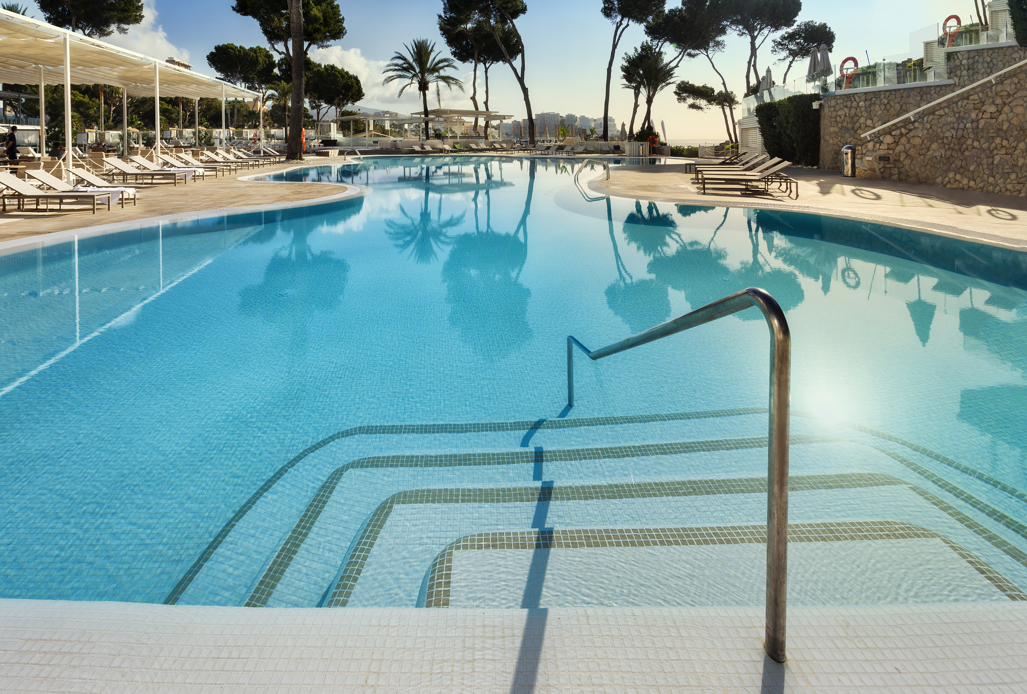 Sunny luxury resort swimming pool with lounge chairs and palm trees.