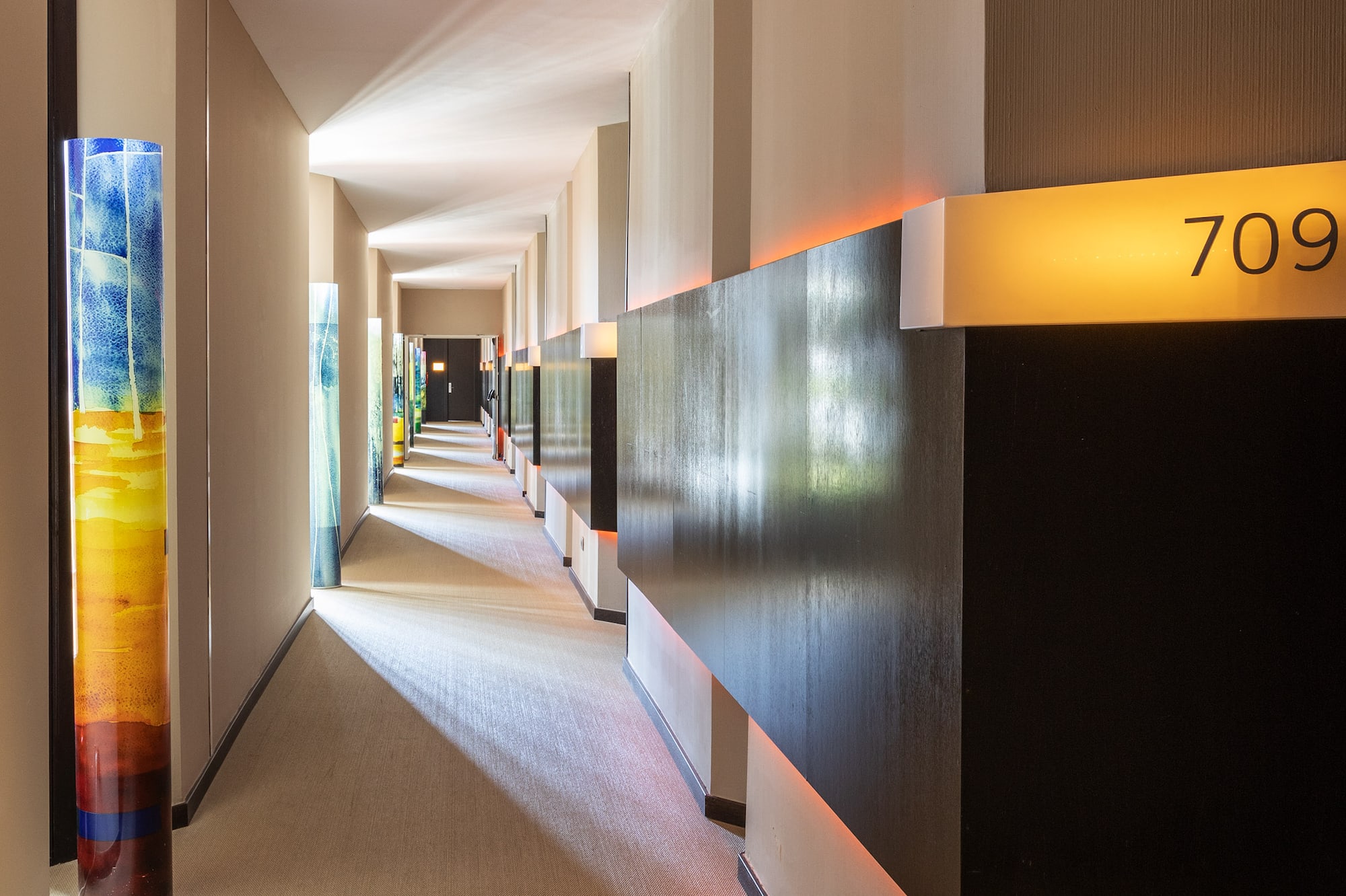 Modern hotel hallway with room 709, colorful art pillars, and warm accent lighting.