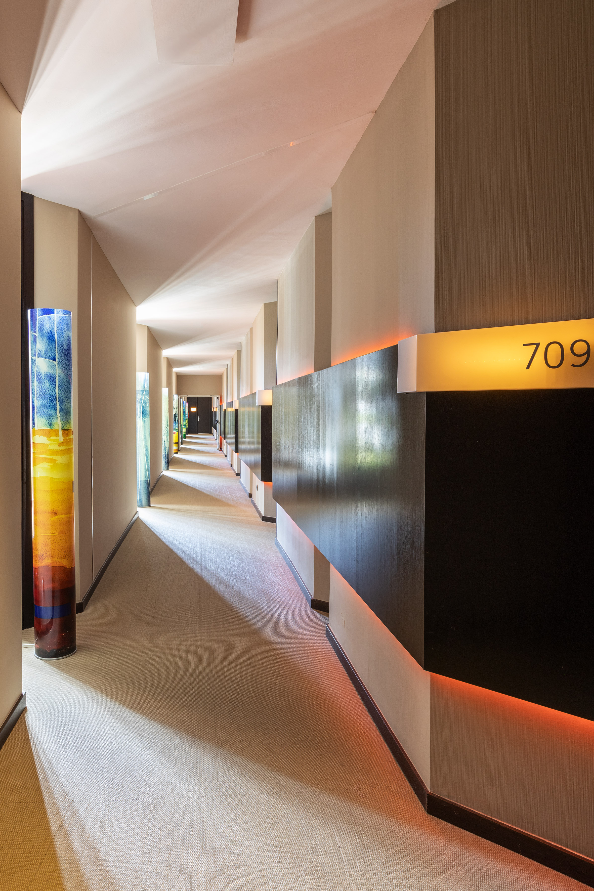 Modern hotel hallway with room 709, colorful art pillars, and warm accent lighting.