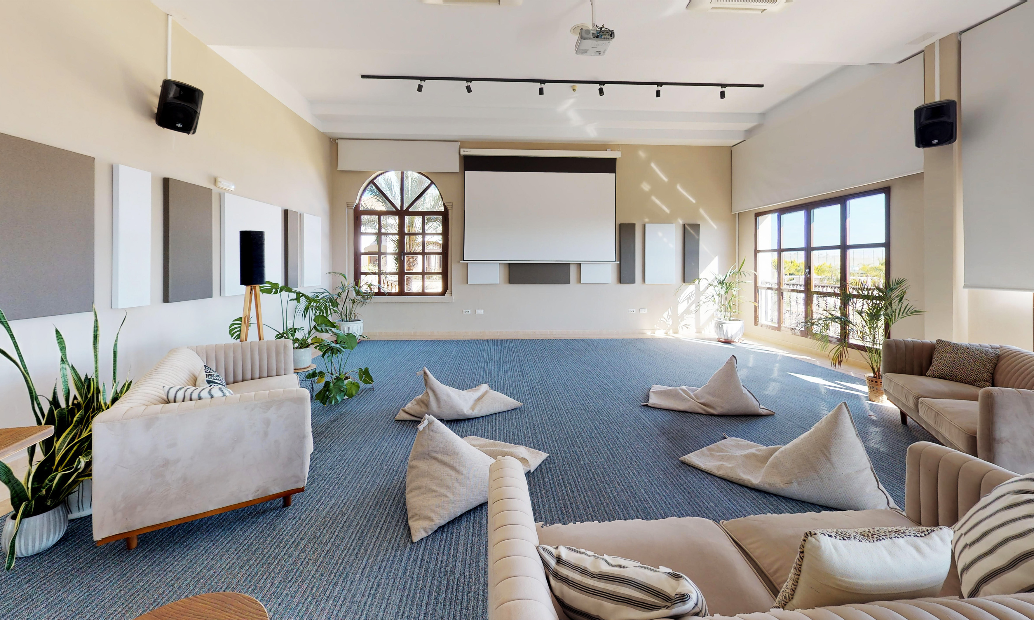 Modern event space with projector screen, soft seating, and blue carpet.
