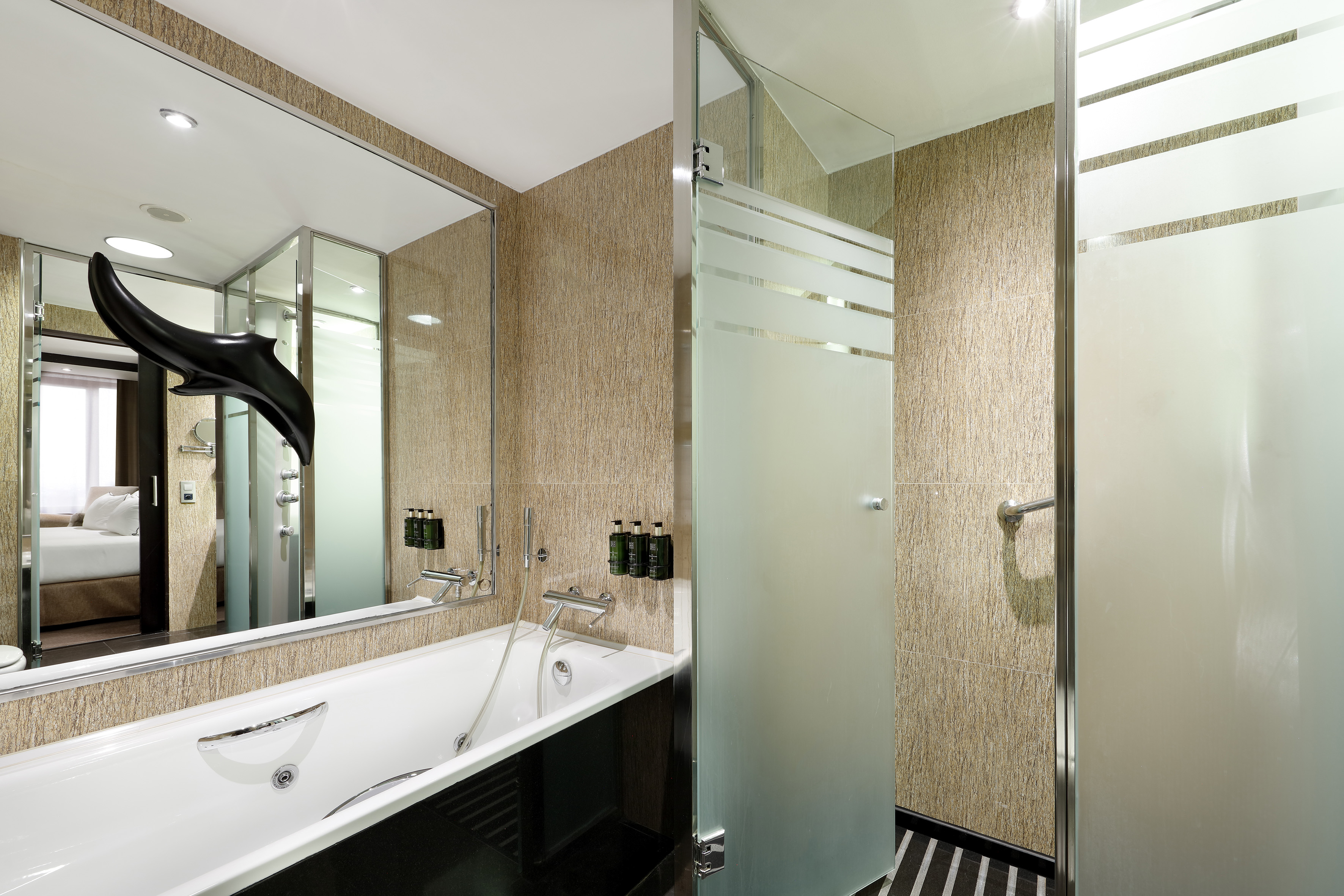 Modern hotel bathroom with jetted tub, walk-in shower, and mirrored bedroom view.