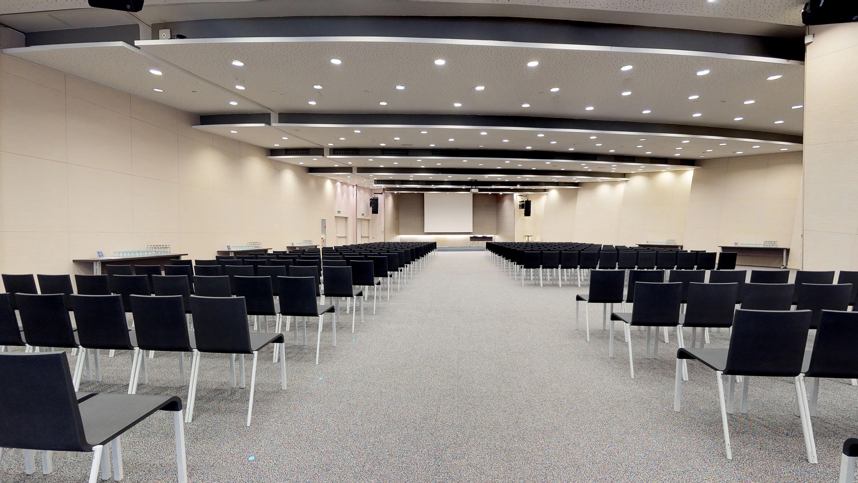 Empty modern conference hall with black chairs, stage, and screen.