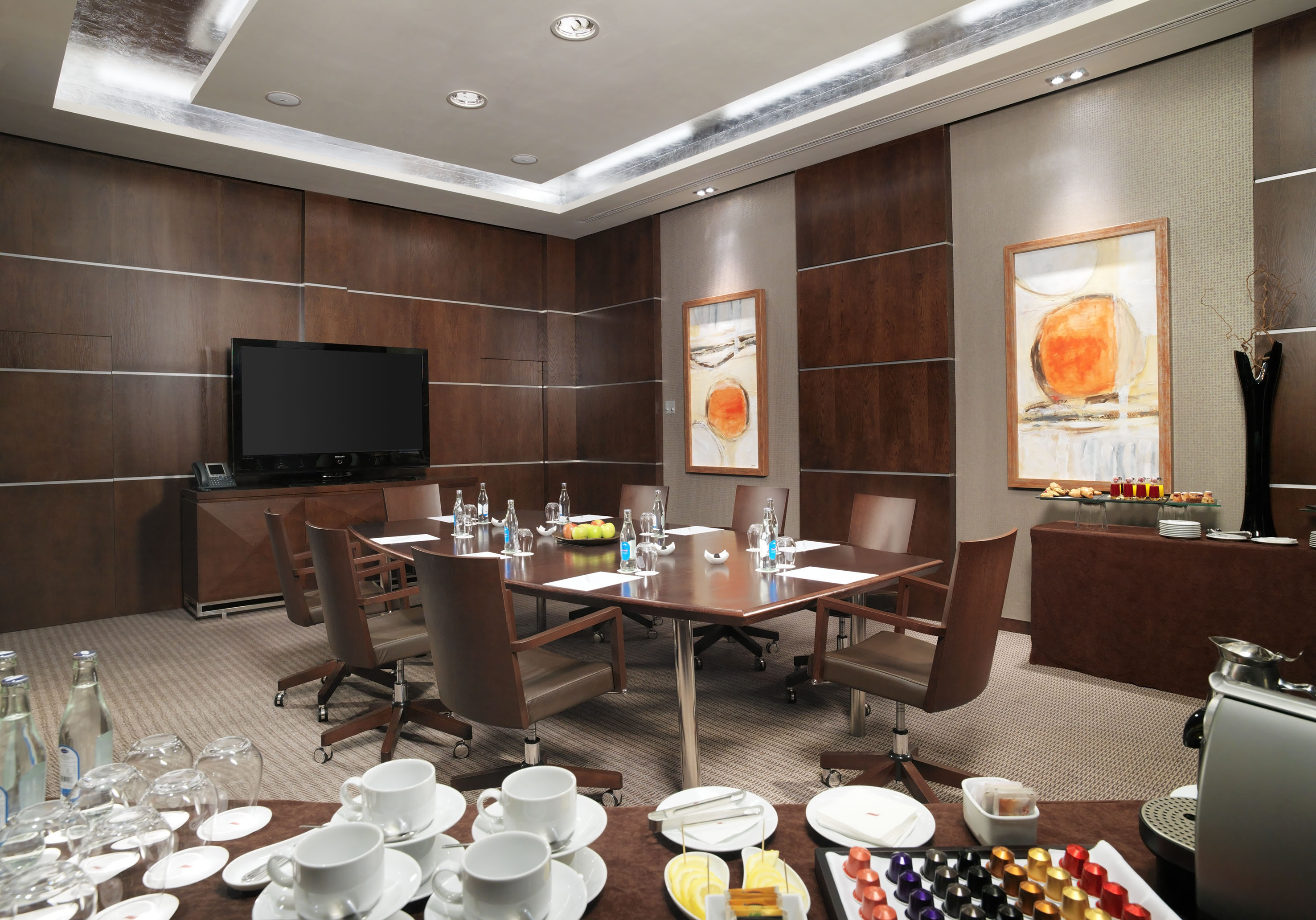 Professional wooden meeting room with conference table, TV, and refreshments.
