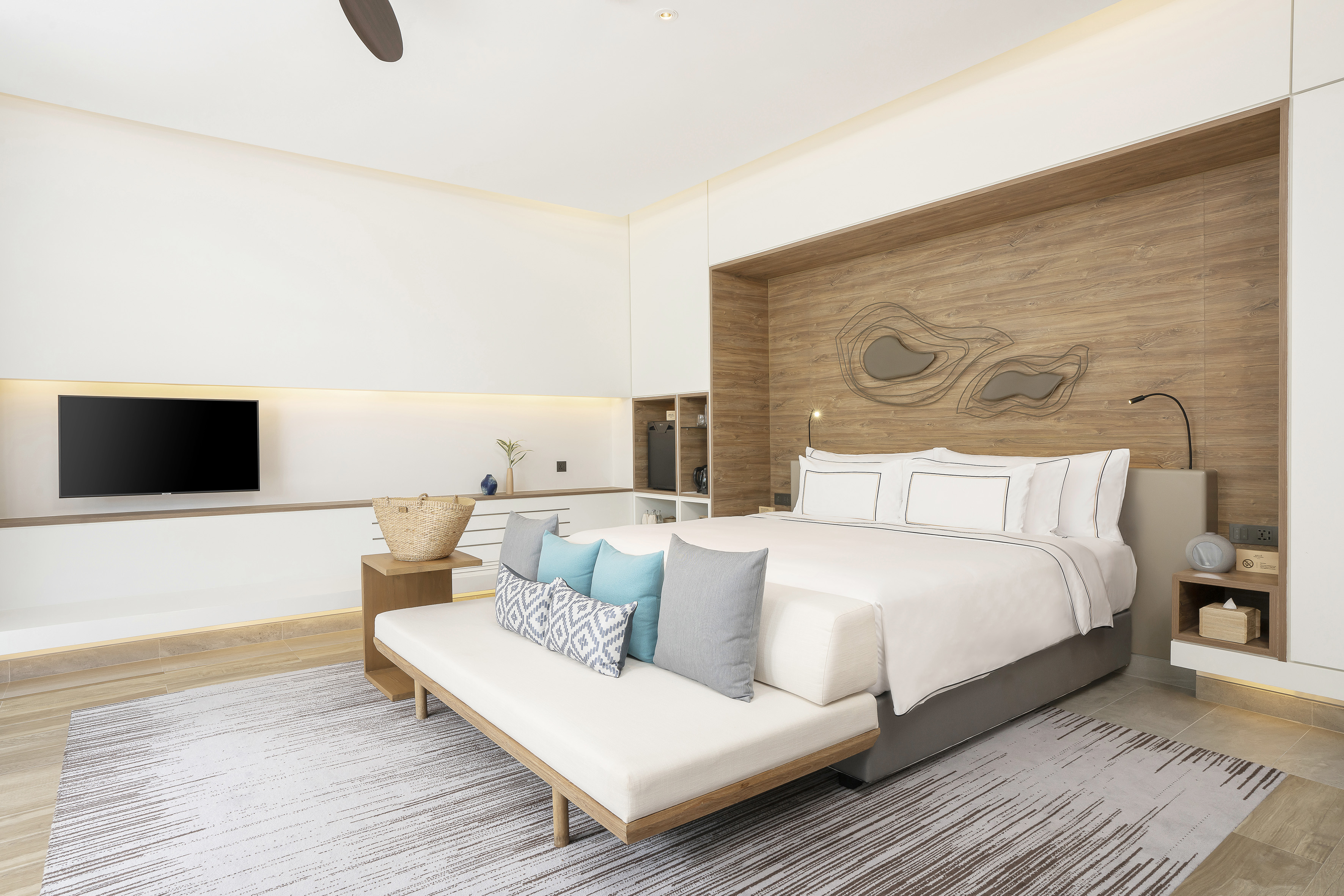 Contemporary hotel bedroom with king bed, wood headboard, TV, and area rug.