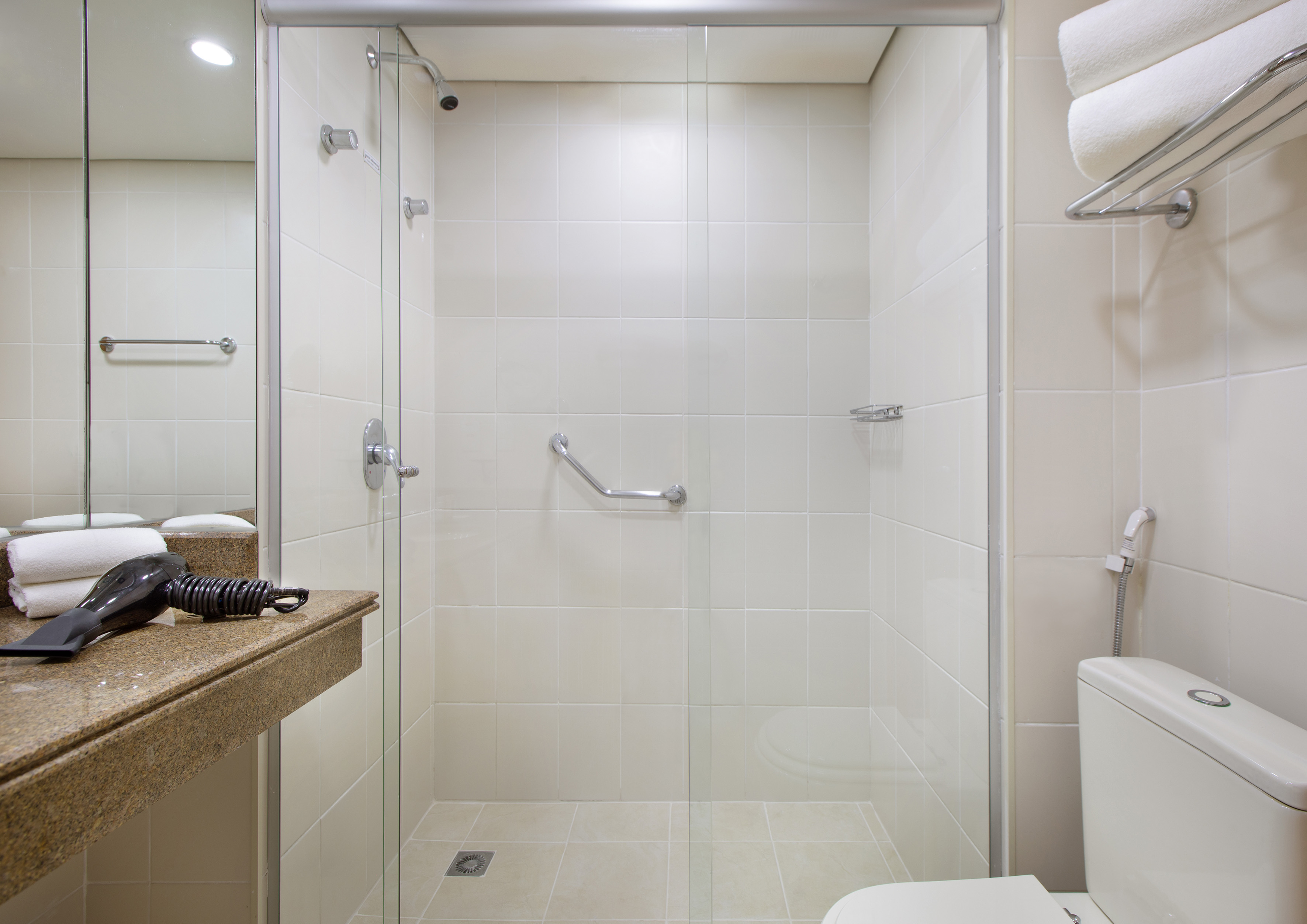 Hotel bathroom with glass shower, grab bar, toilet, and granite vanity.
