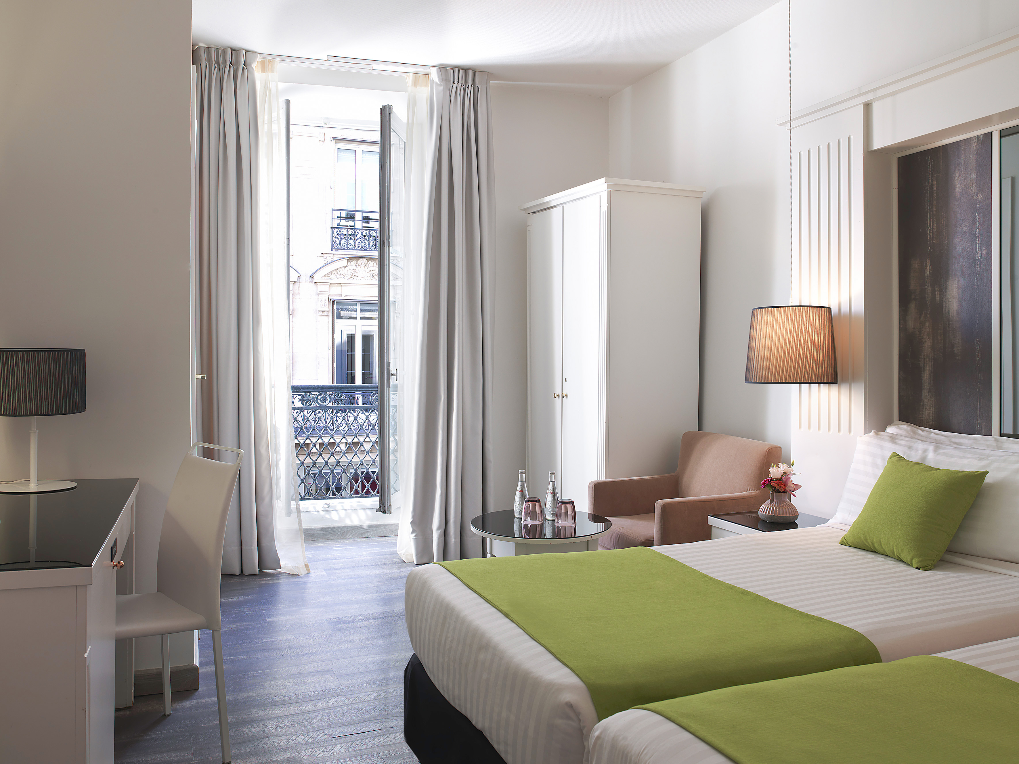 Hotel room with twin beds, green accents, desk, and balcony city view.
