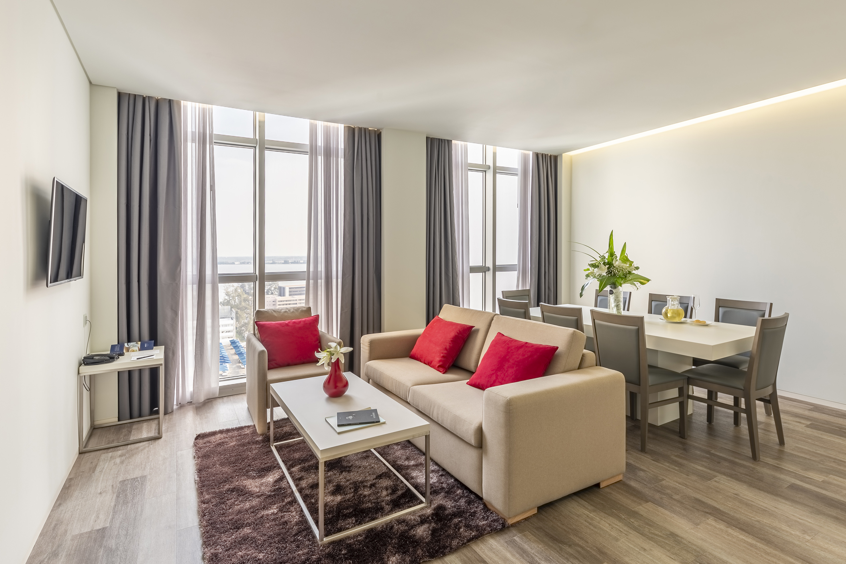 Modern living room, dining area, beige sofa, red pillows, large windows.