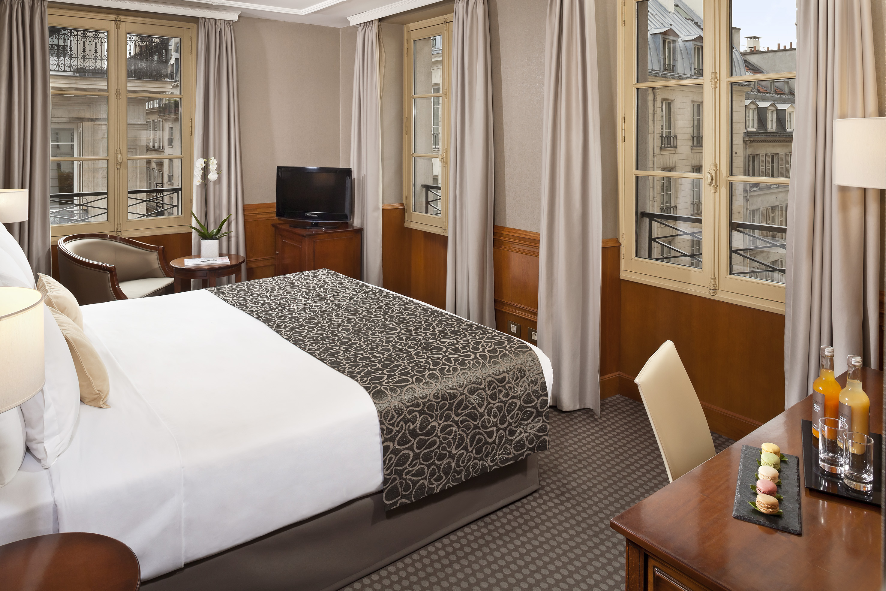 Hotel room with Parisian city view, comfortable bed, and desk with macarons.